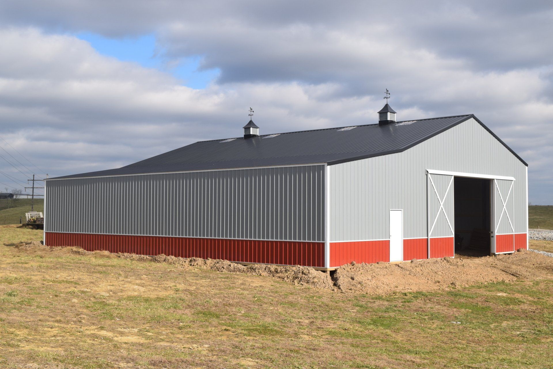 A metal barn with a grey and red exterior under a cloudy sky in a field.