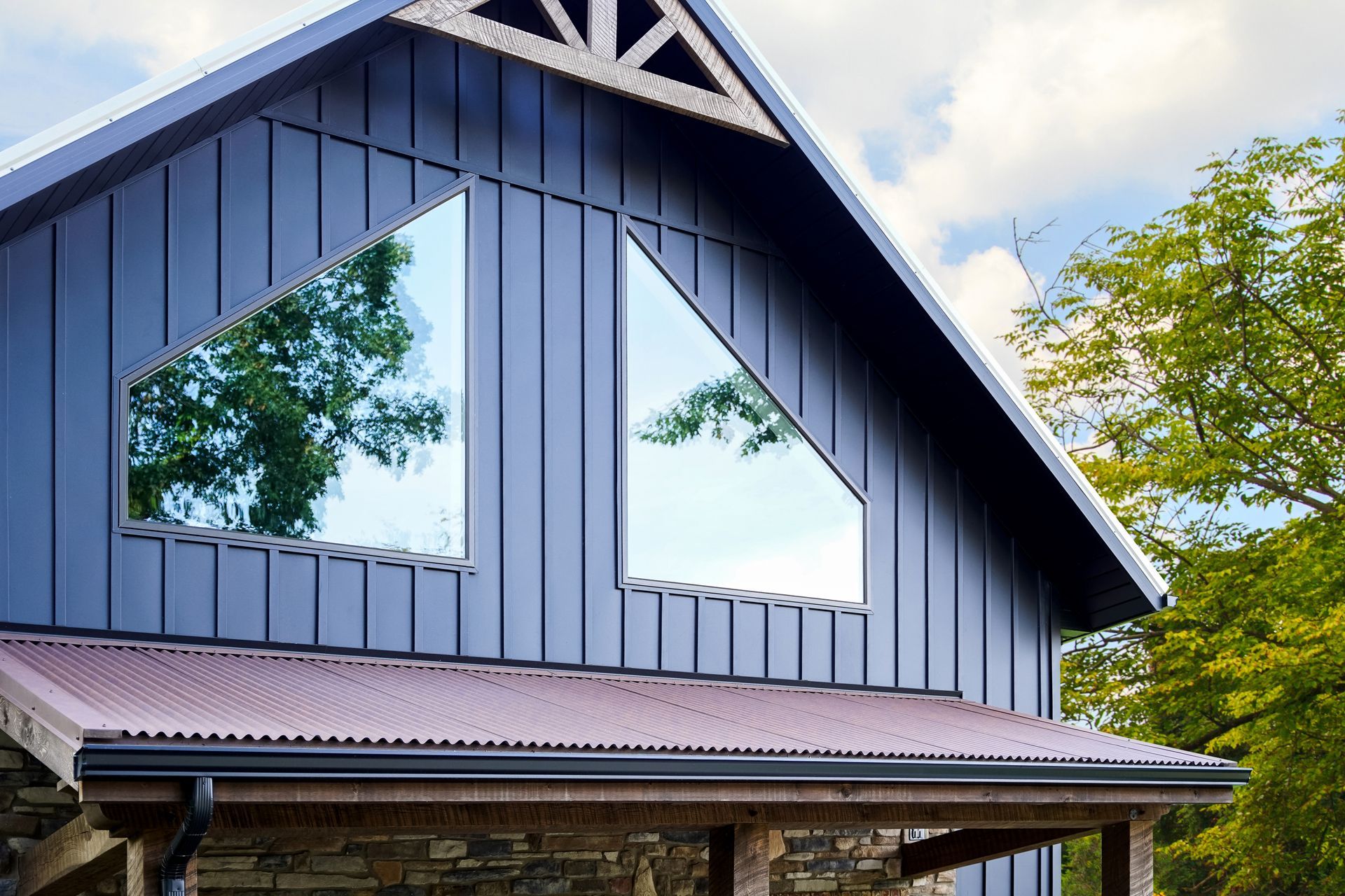 A modern building exterior featuring vertical blue siding, a corrugated roof, and two angular, reflective windows.