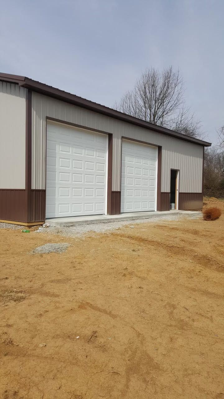 A metal-sided building with two white garage doors and a side door, situated on a dirt lot under a blue sky.