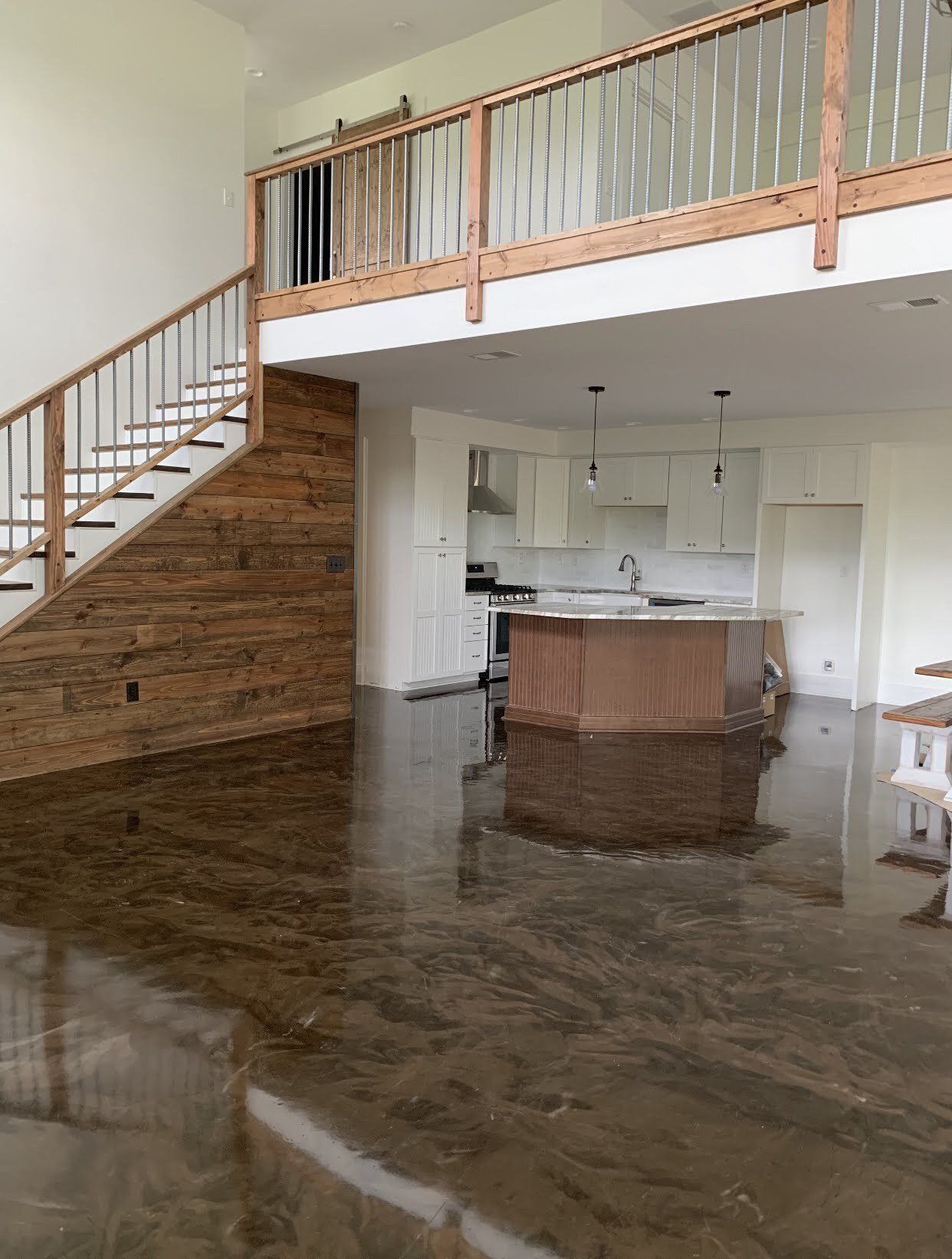 An open-concept living area with a staircase, a wooden accent wall, and a kitchen visible under a lofted second floor.