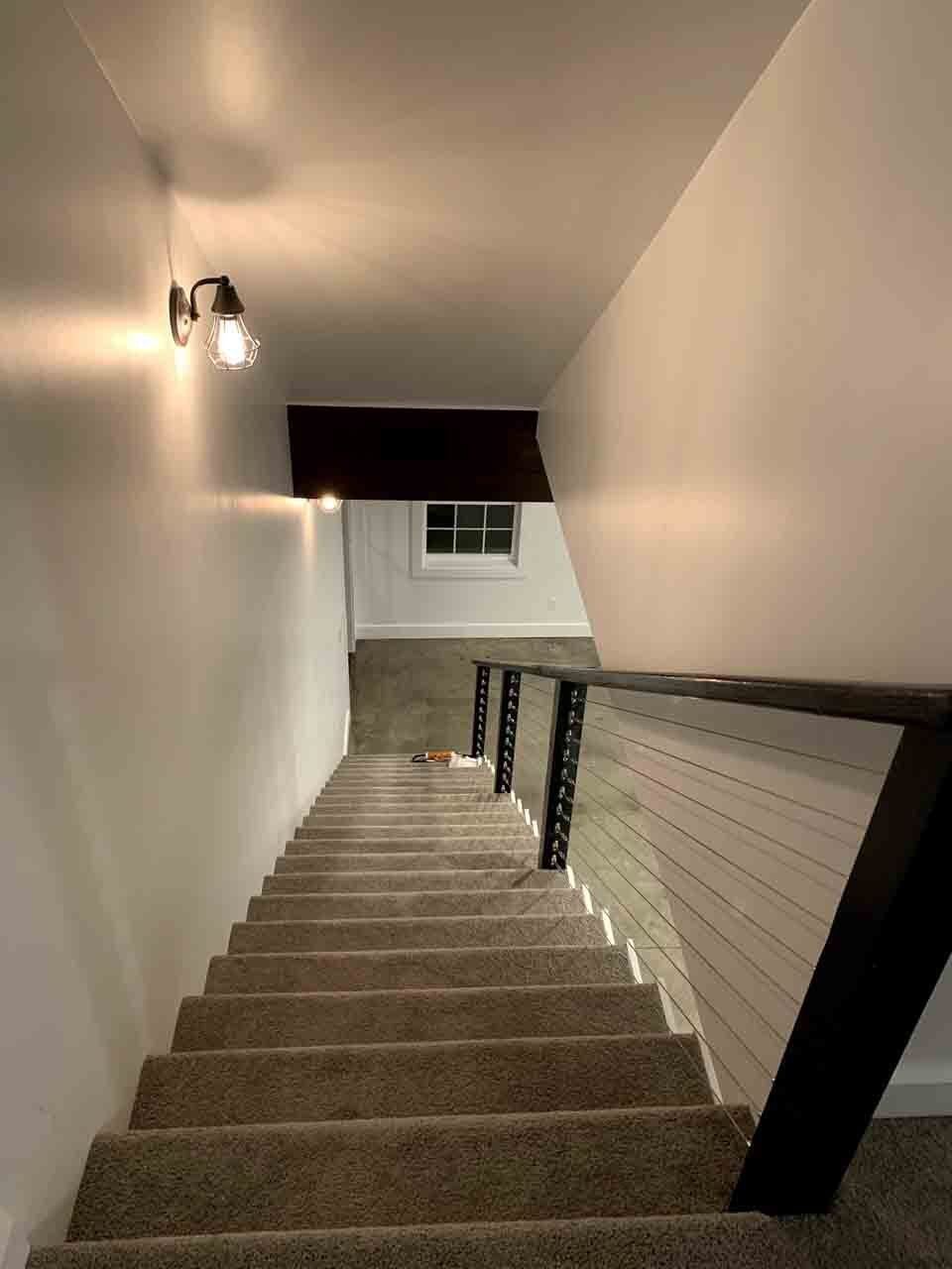 A carpeted staircase descends between white walls with a dark wood handrail and a wall-mounted light fixture.