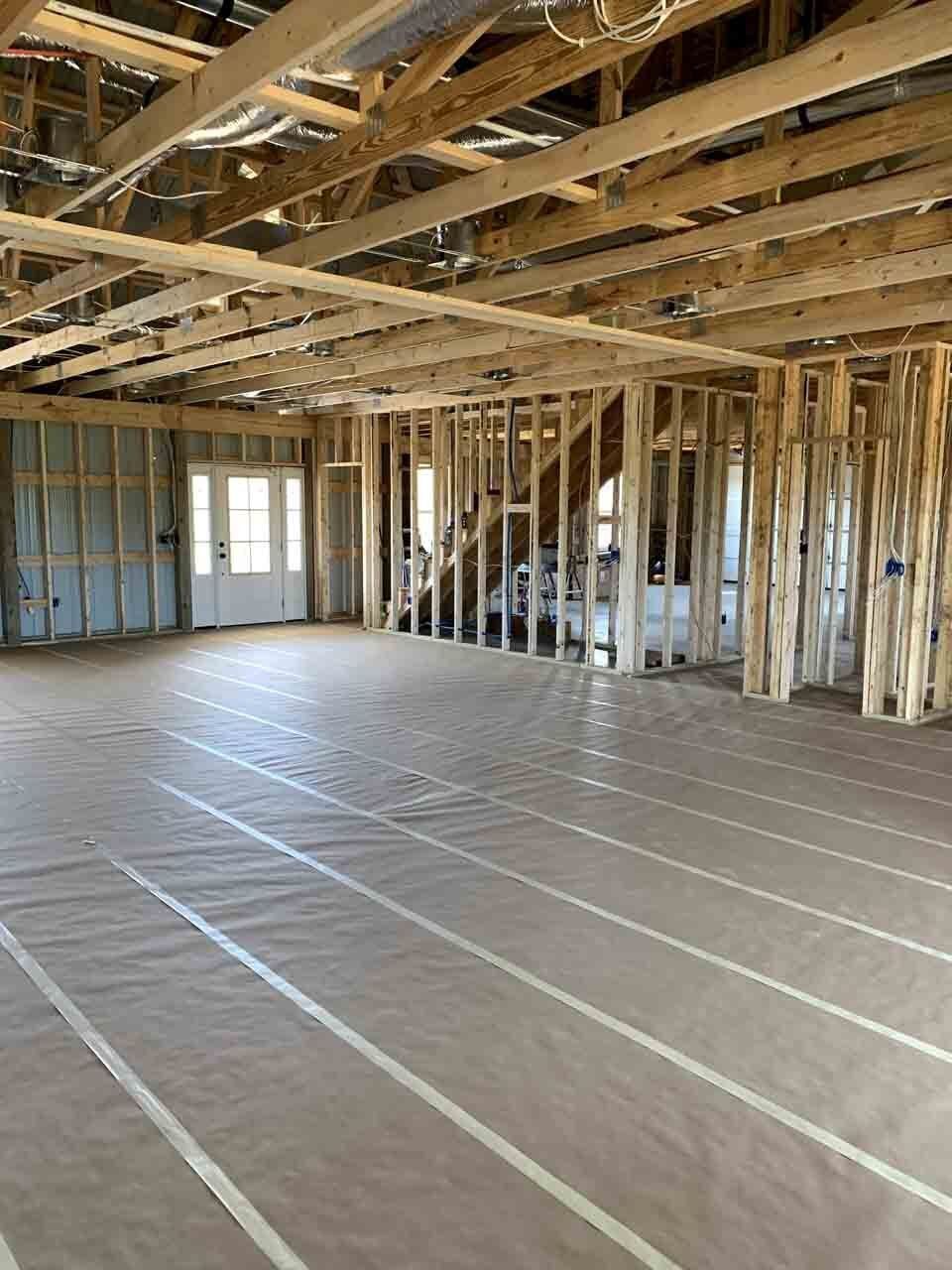 An unfinished interior room with exposed wooden framing and a floor covered in protective brown paper and white tape.