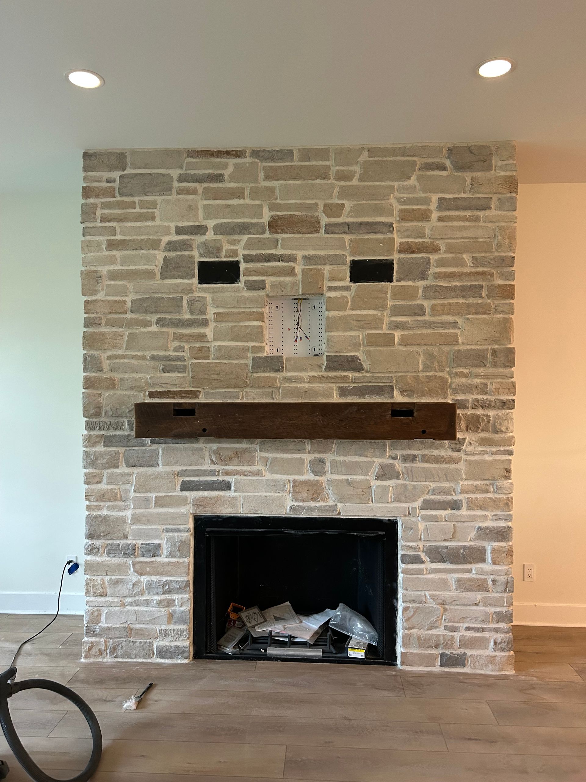 A stone fireplace feature wall with a dark wood mantel and a television mount attached.