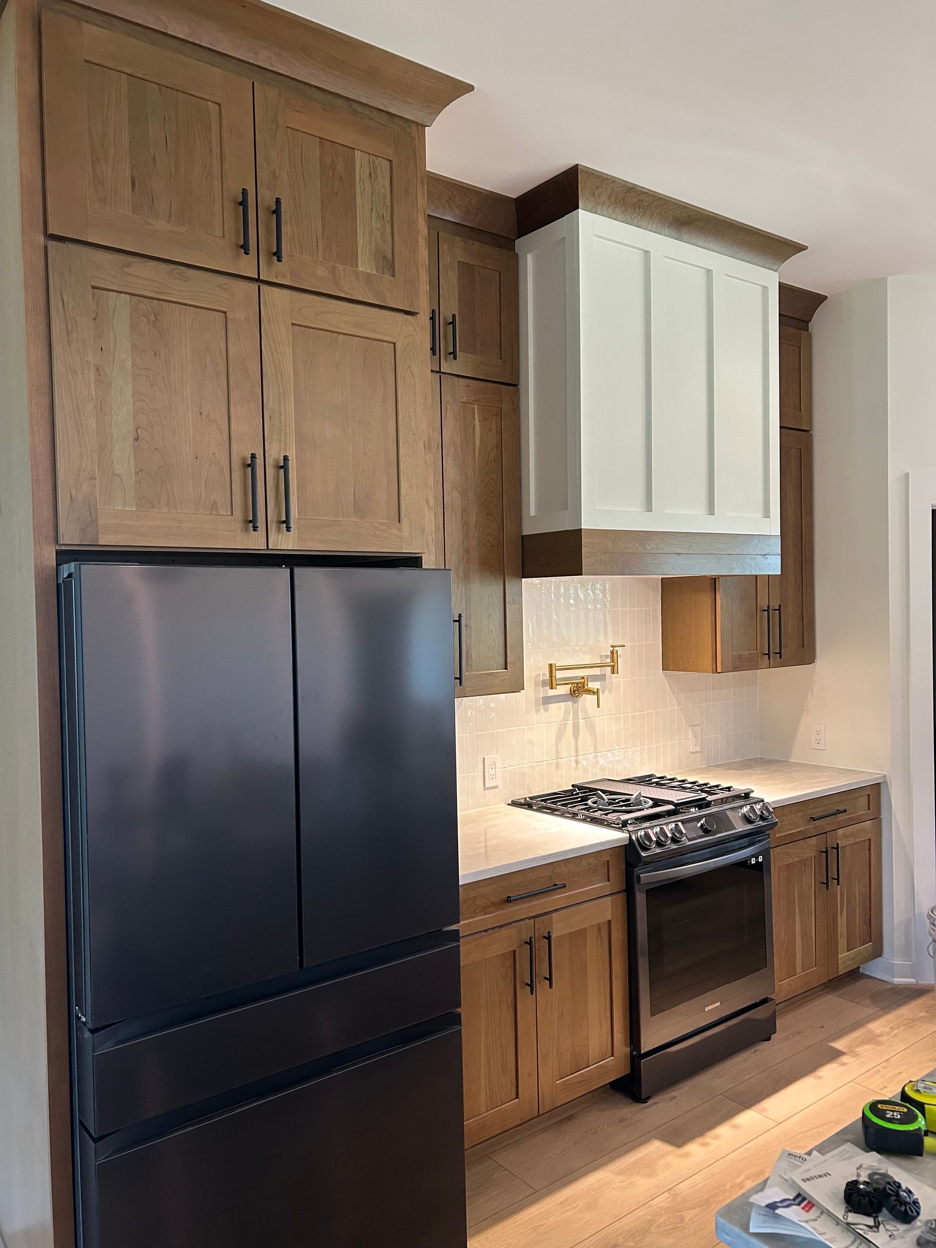 A modern kitchen with wood cabinets, a black refrigerator, a white range hood, and stainless steel appliances.