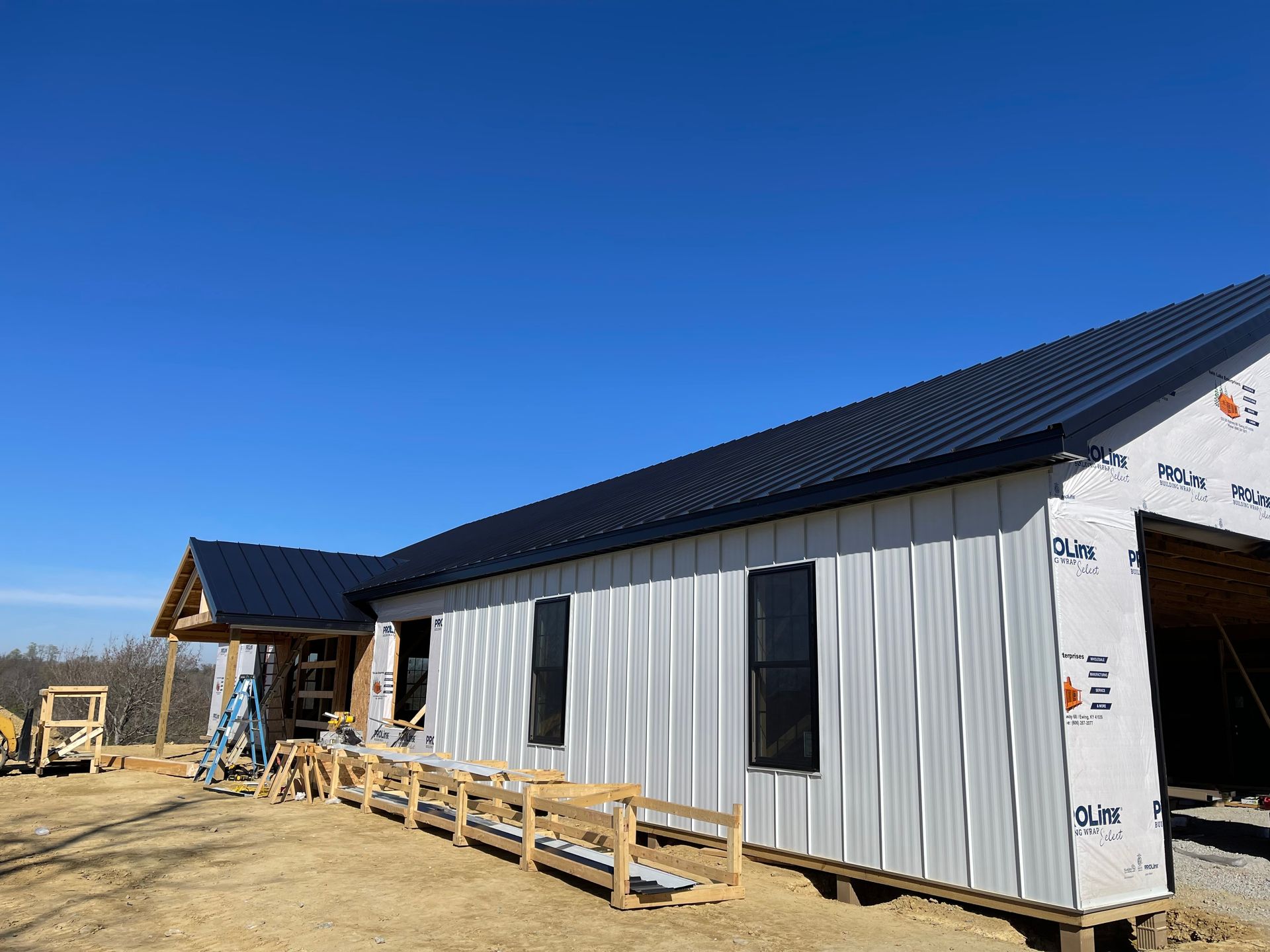 A new white metal-sided building under construction with a dark roof against a clear blue sky.