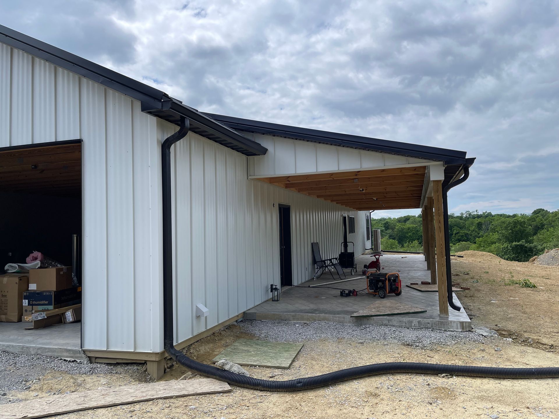 A side view of a white, board-and-batten style building under construction with a covered patio and a black downspout.