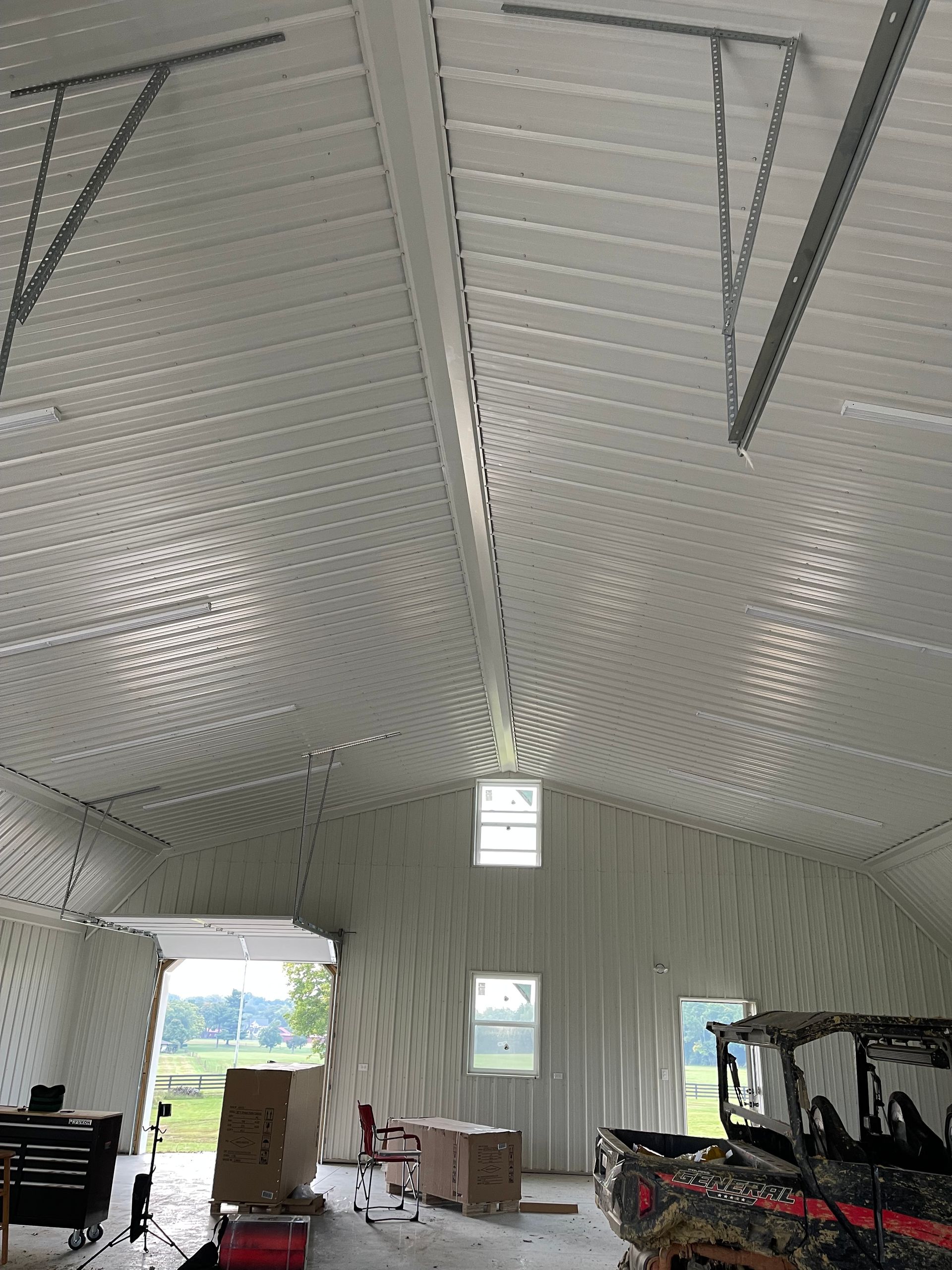 Interior view of a spacious garage with curved, white metal walls and ceiling, two windows, and parked utility vehicles.