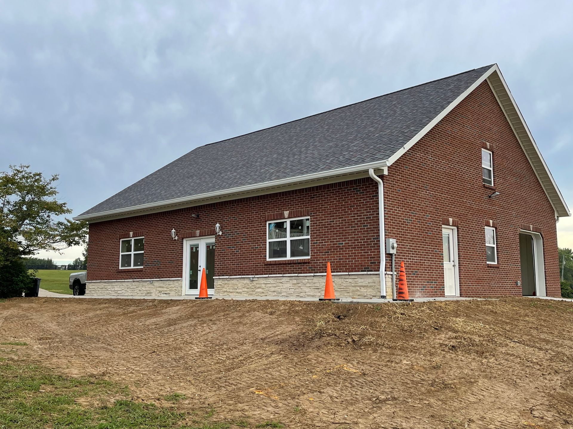 A red brick house with a dark shingled roof and stone base, featuring multiple doors and windows under a cloudy sky.