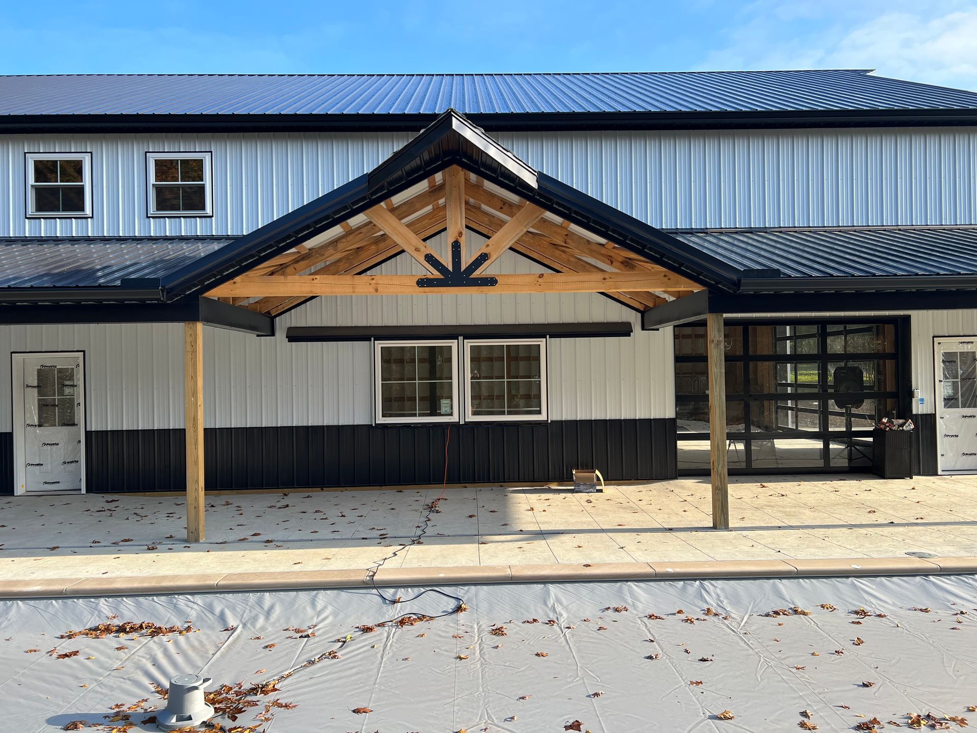 A white building with black trim features a wooden A-frame entrance canopy and a large glass-paned garage door.