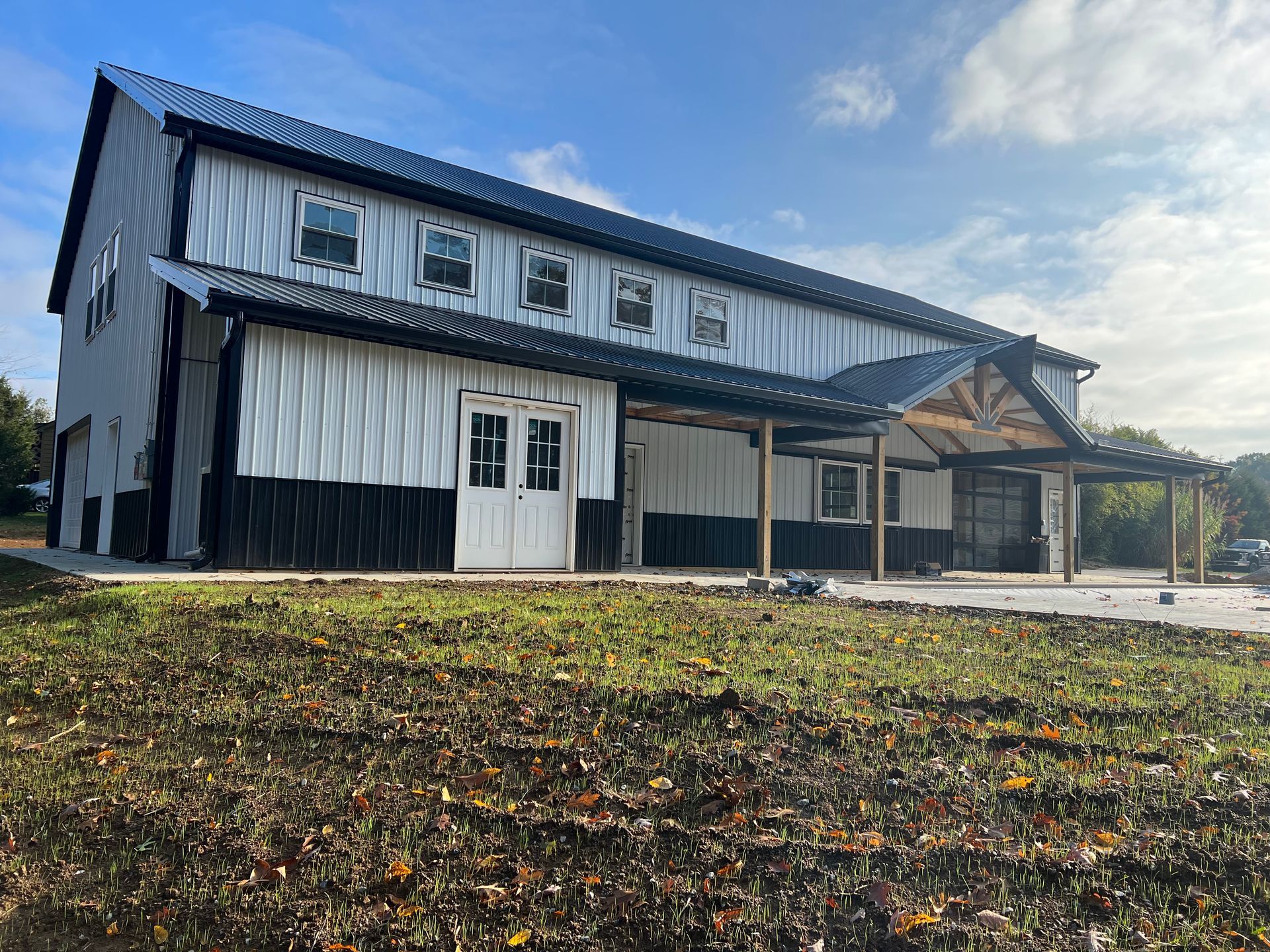 A modern white and black metal-sided barn-style building with a covered porch under a sunny blue sky.