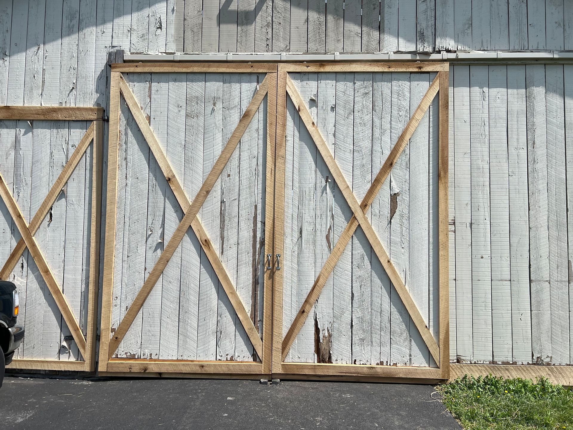 Two large white wooden barn doors with natural wood diagonal bracing sit on a dark paved surface.