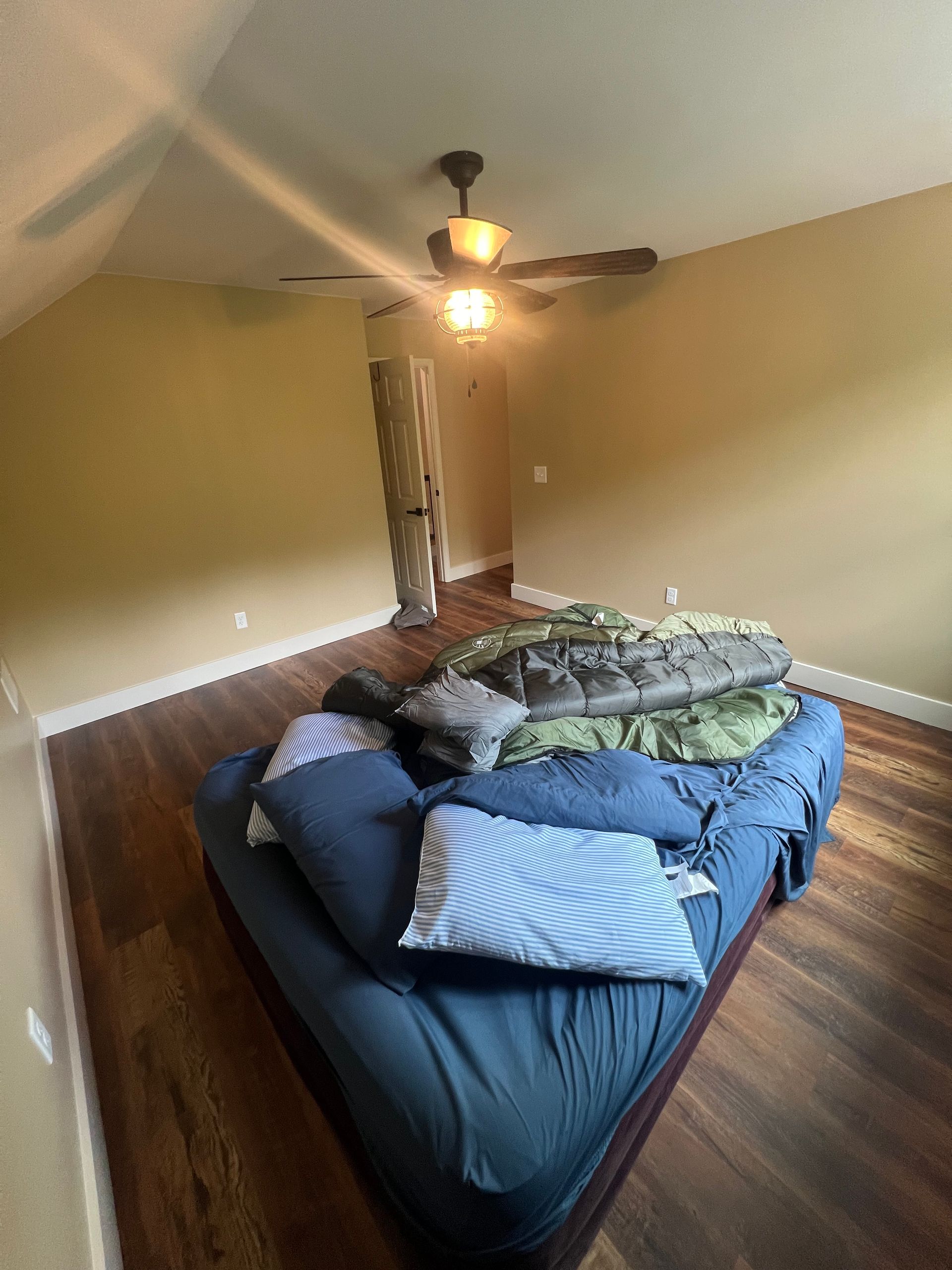 A mattress on a hardwood floor in a room with tan walls and a ceiling fan.