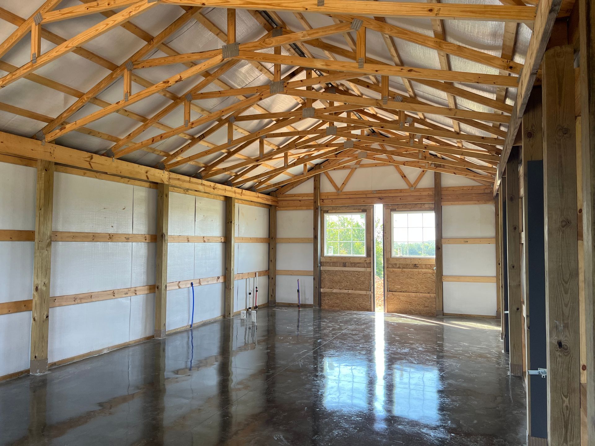 Interior of a pole barn with exposed wooden trusses, white-lined walls, and a polished, reflective concrete floor.