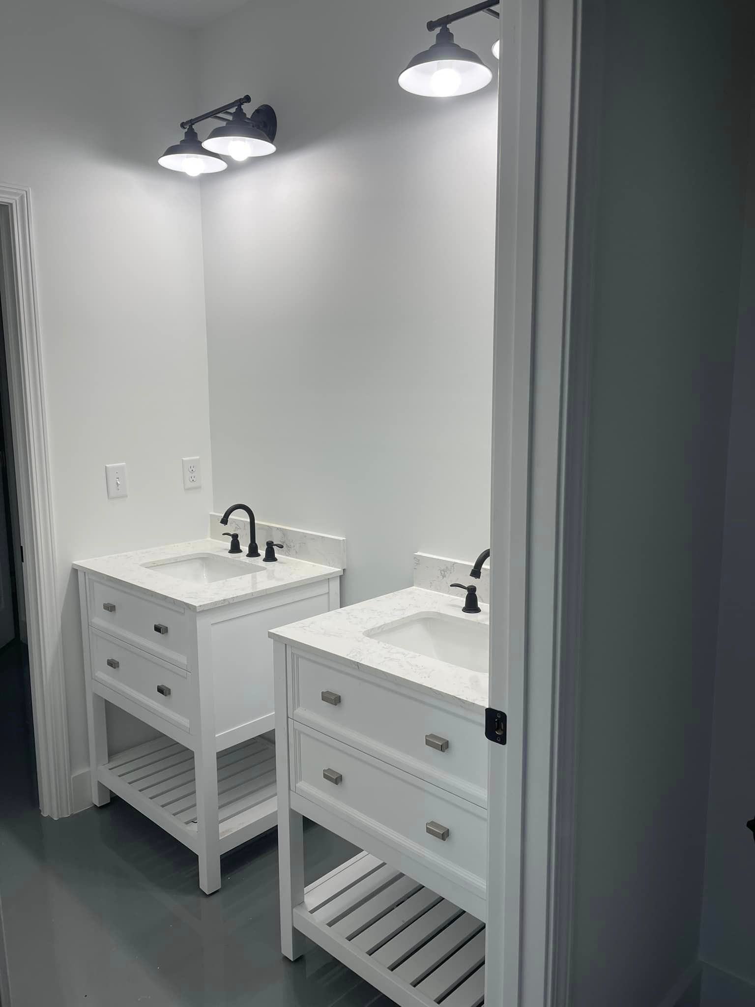 A bathroom vanity area featuring two white pedestal sinks with black faucets, under-counter storage, and overhead lighting.
