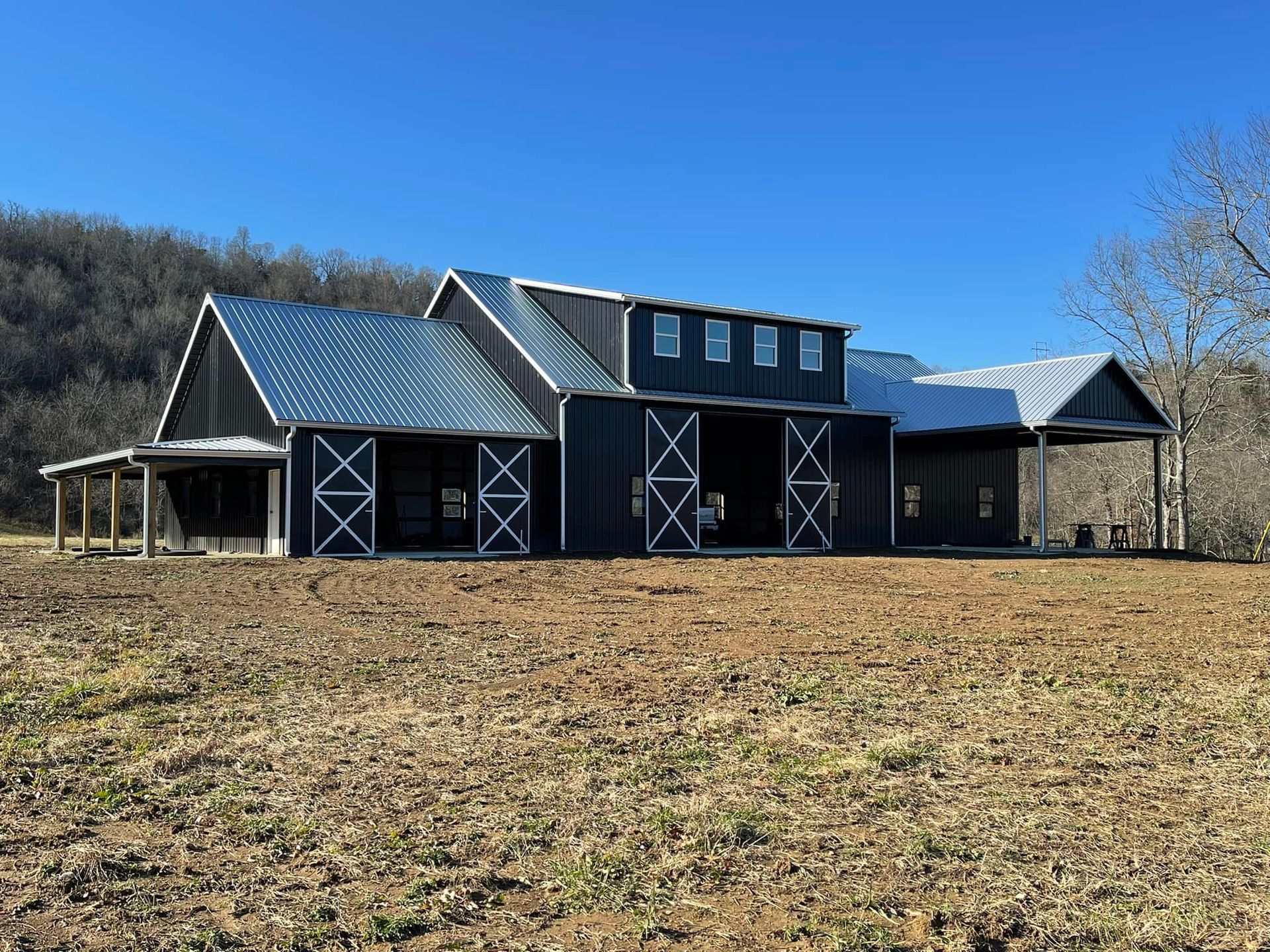 A black barn with white trim and a silver metal roof sits in a field under a clear blue sky.