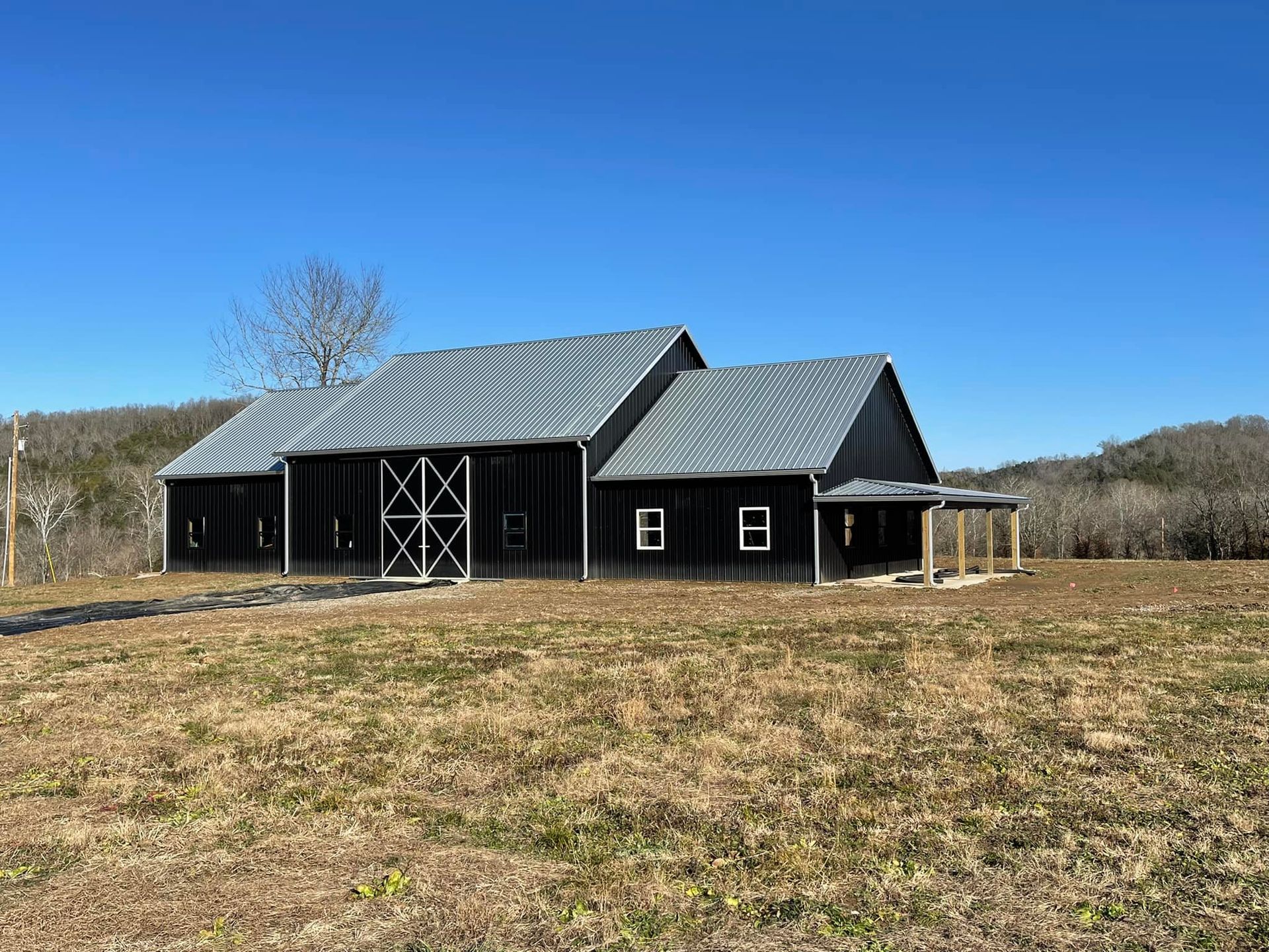 A dark-sided barn with a metallic roof sits in a dry, grassy field under a clear blue sky.