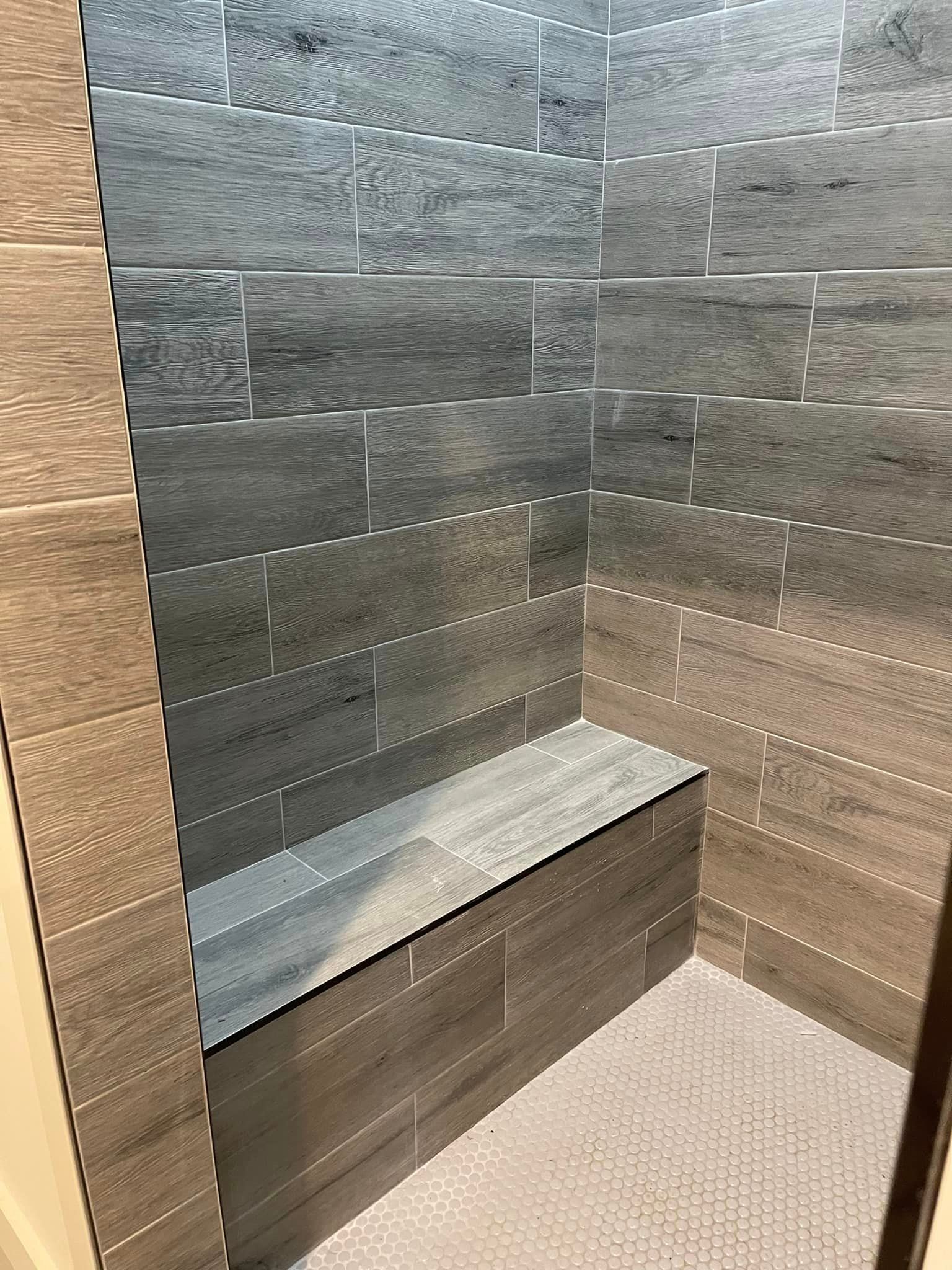A shower interior featuring grey textured tile walls, a built-in bench, and a small-patterned white tile floor.