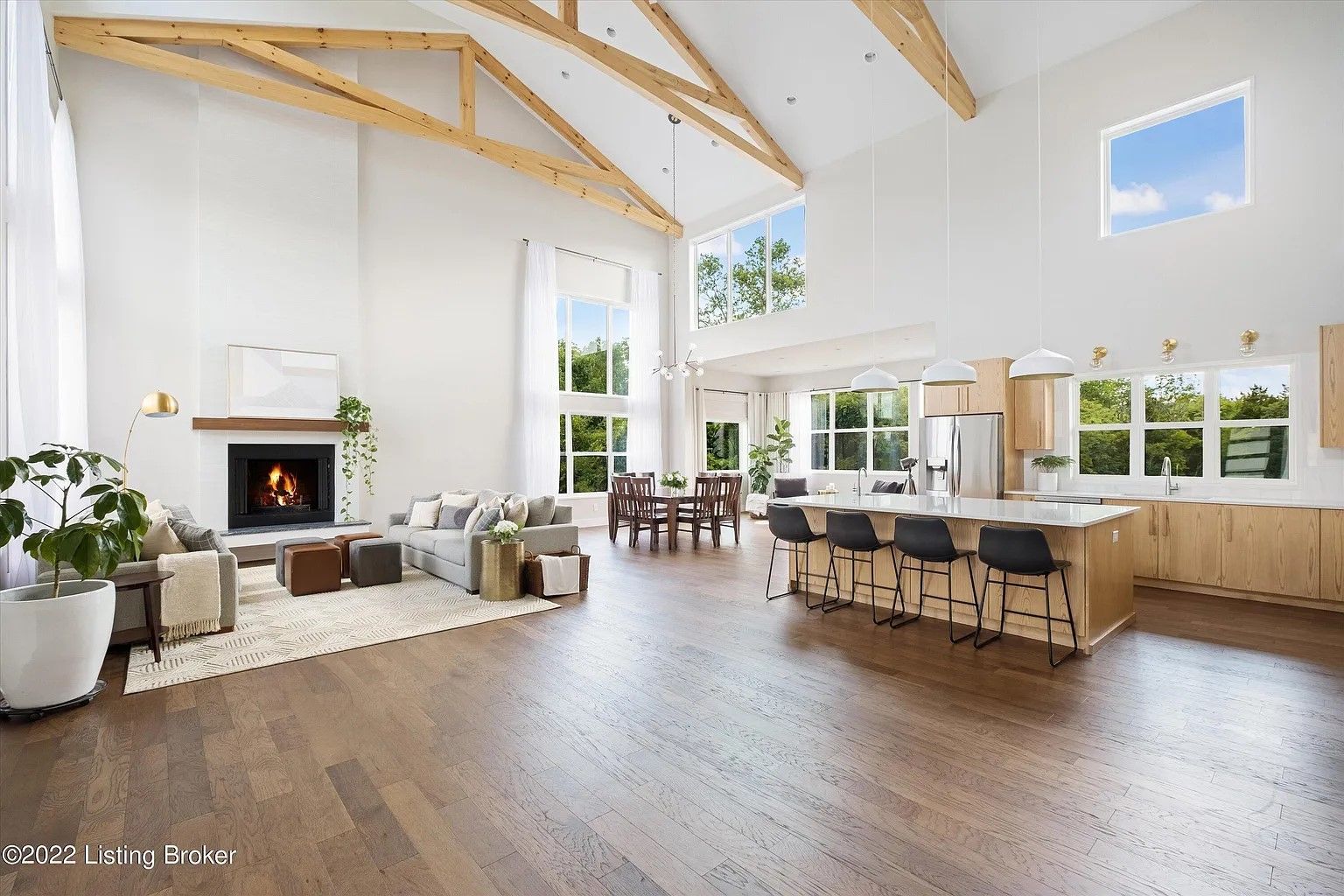 Open-concept great room with vaulted ceilings, exposed timber beams, a stone fireplace, and a large kitchen island.