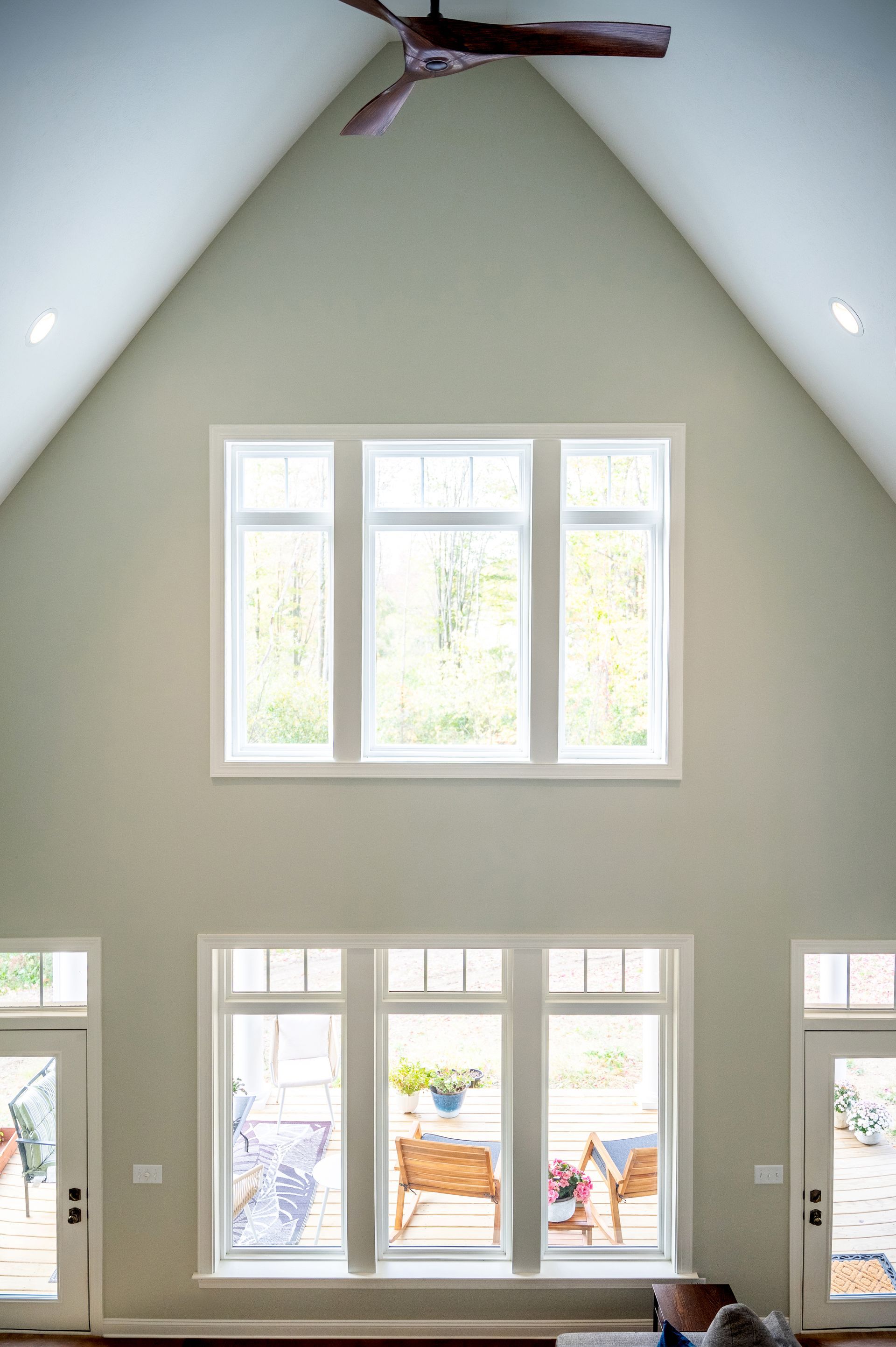 A light-colored room with a high vaulted ceiling, large windows in two tiers, and a wooden ceiling fan.