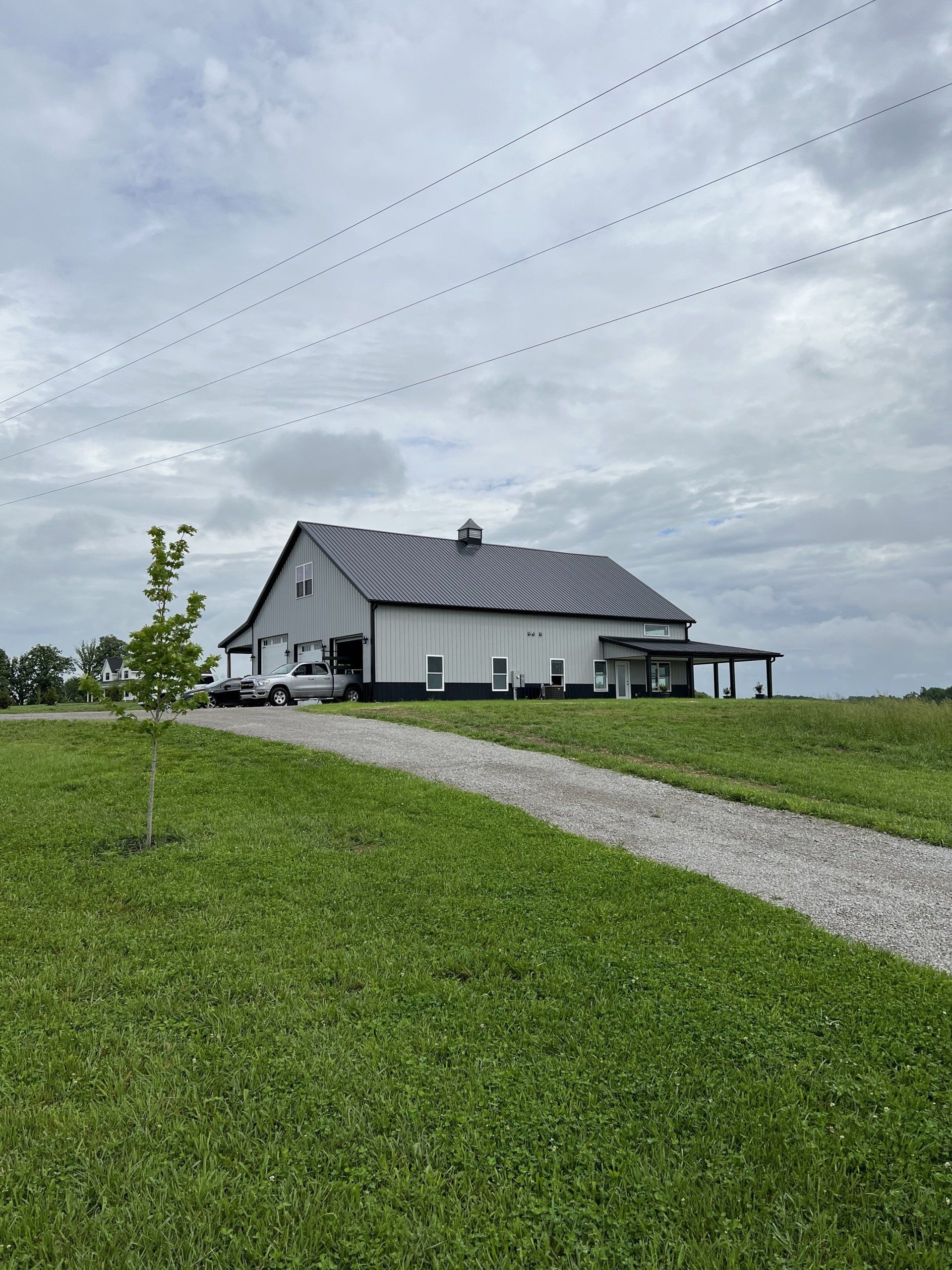 A gray-roofed white building stands on a grassy hill next to a gravel driveway under a cloudy sky.