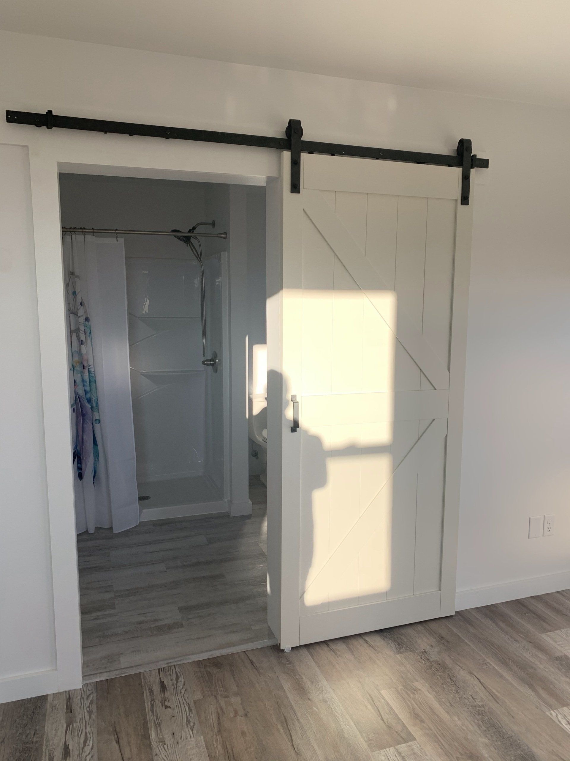 A white sliding barn door with geometric patterns, mounted on a black metal track, opens into a bright bathroom.
