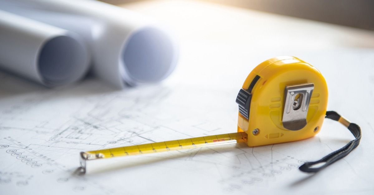 A tabletop with blueprints, rolled plans, and a yellow measuring tape arranged for building project 