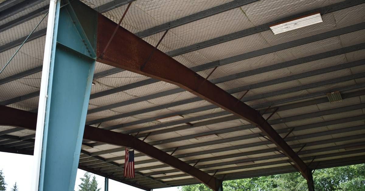 An upward view of a pole barn structure's roof. The steel bars supporting it are painted teal blue and the roof is beige.