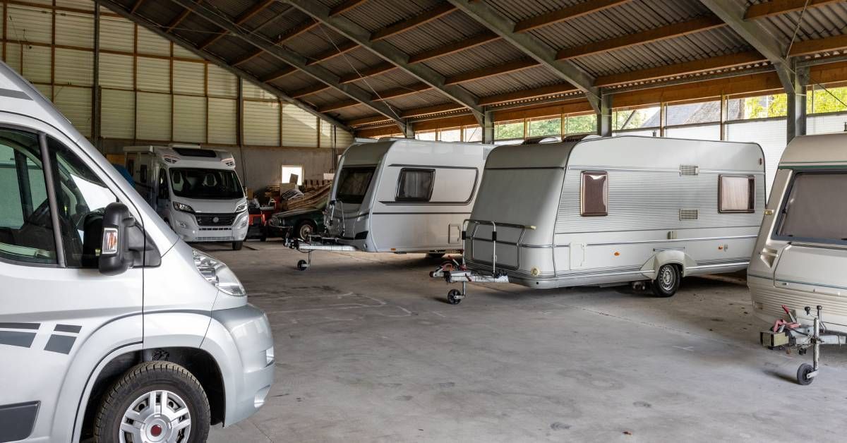 Several RV trailers stored in a barn with protection from the outdoors. The RVs are mainly white with some accents.