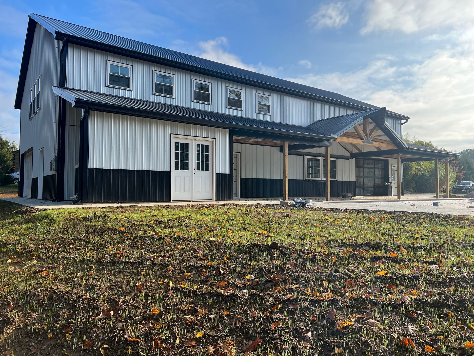 A modern two-story barn-style building with white and black metal siding, a covered patio, and a metal roof.