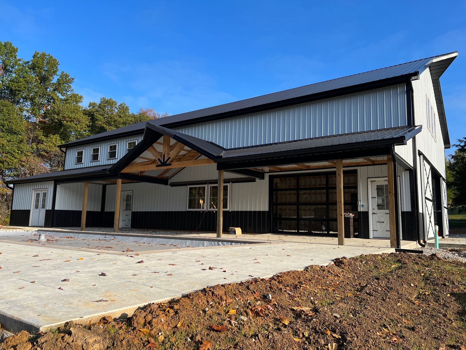 A white and black metal barndominium-style building with a covered entryway, a glass garage door, and a concrete patio.