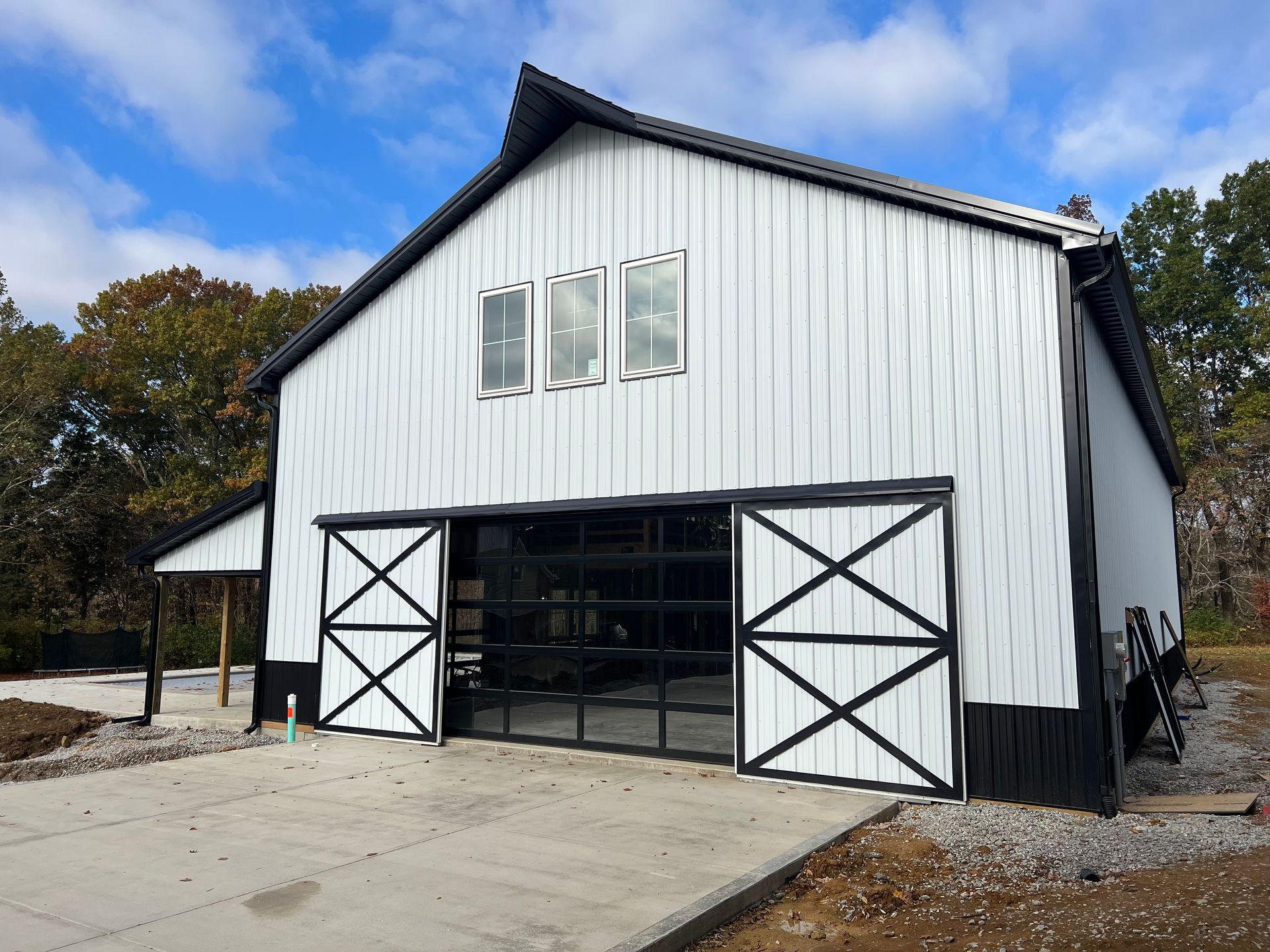 A white barn with black trim, sliding barn doors, a central glass garage door, and three windows under a gabled roof.