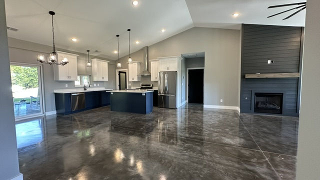 Open-plan kitchen and living area with polished concrete floors, dark blue cabinets, white countertops, and a fireplace.