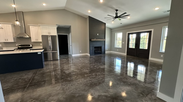 A modern open-plan living room and kitchen with polished concrete floors, a dark fireplace accent wall, and glass doors.