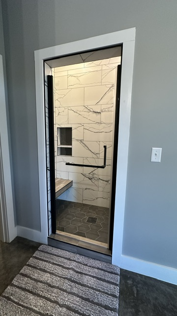 A glass shower door with a black frame and handle, featuring marble-style wall tiles and dark floor tiles inside.
