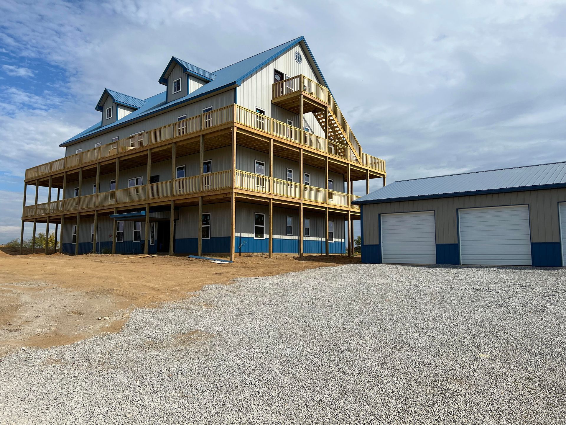 A three-story building with wraparound wooden decks and a blue metal roof stands next to a matching two-car garage.