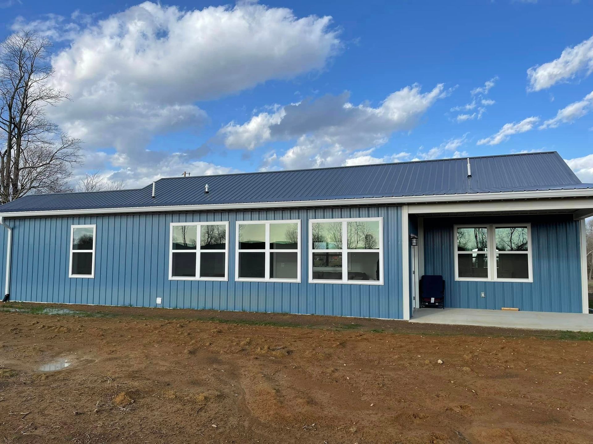 A blue, single-story metal building with a dark roof and multiple windows under a bright, partly cloudy sky.