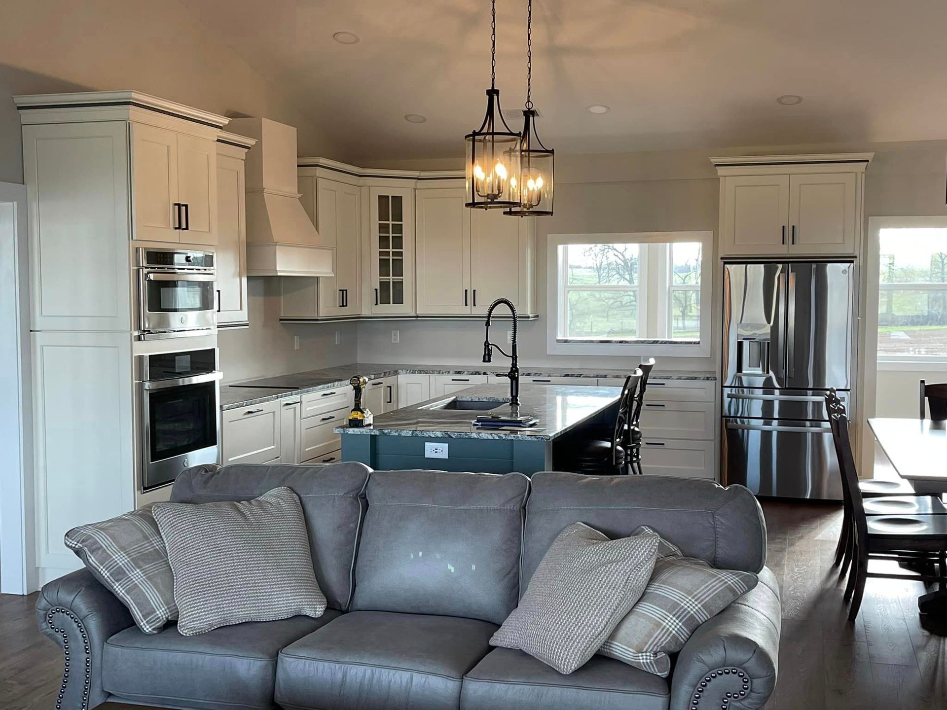 A kitchen with white cabinetry, a central island, stainless steel appliances, and a gray sofa in the foreground.