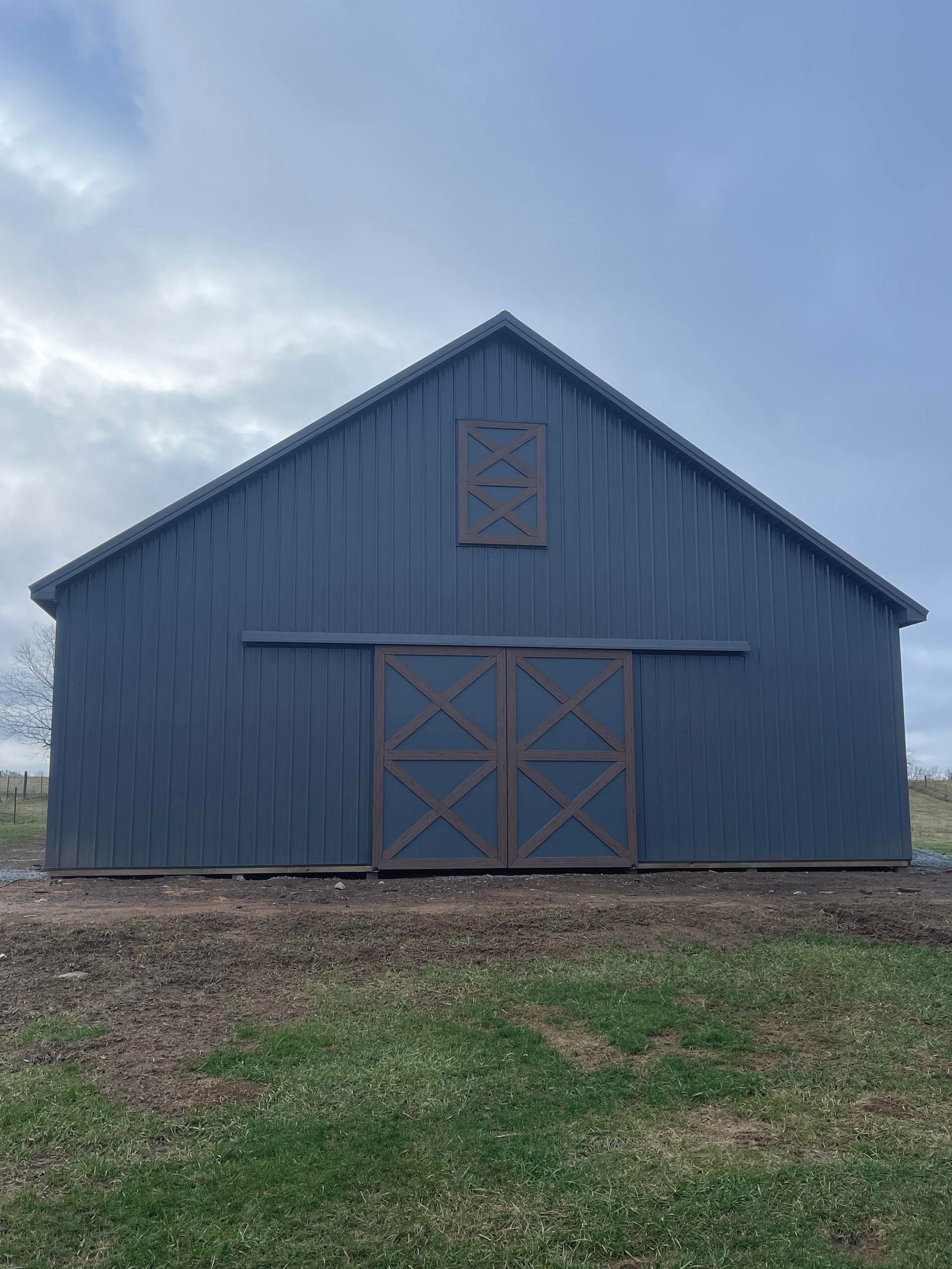 A blue metal-sided barn with double sliding doors and a decorative plaque centered under the roof peak.