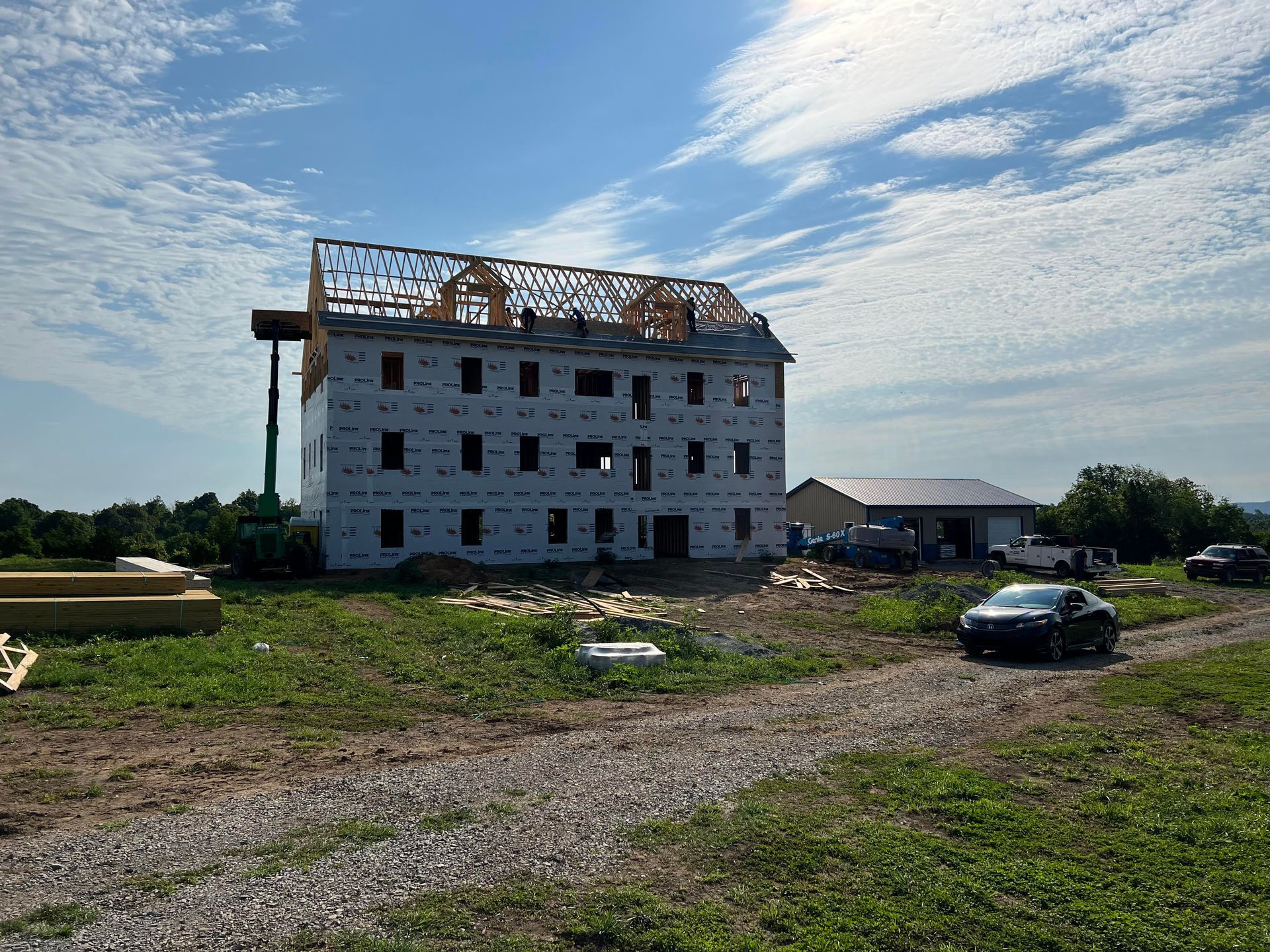 A three-story building under construction with exposed wooden roof trusses, partially covered in white sheathing.