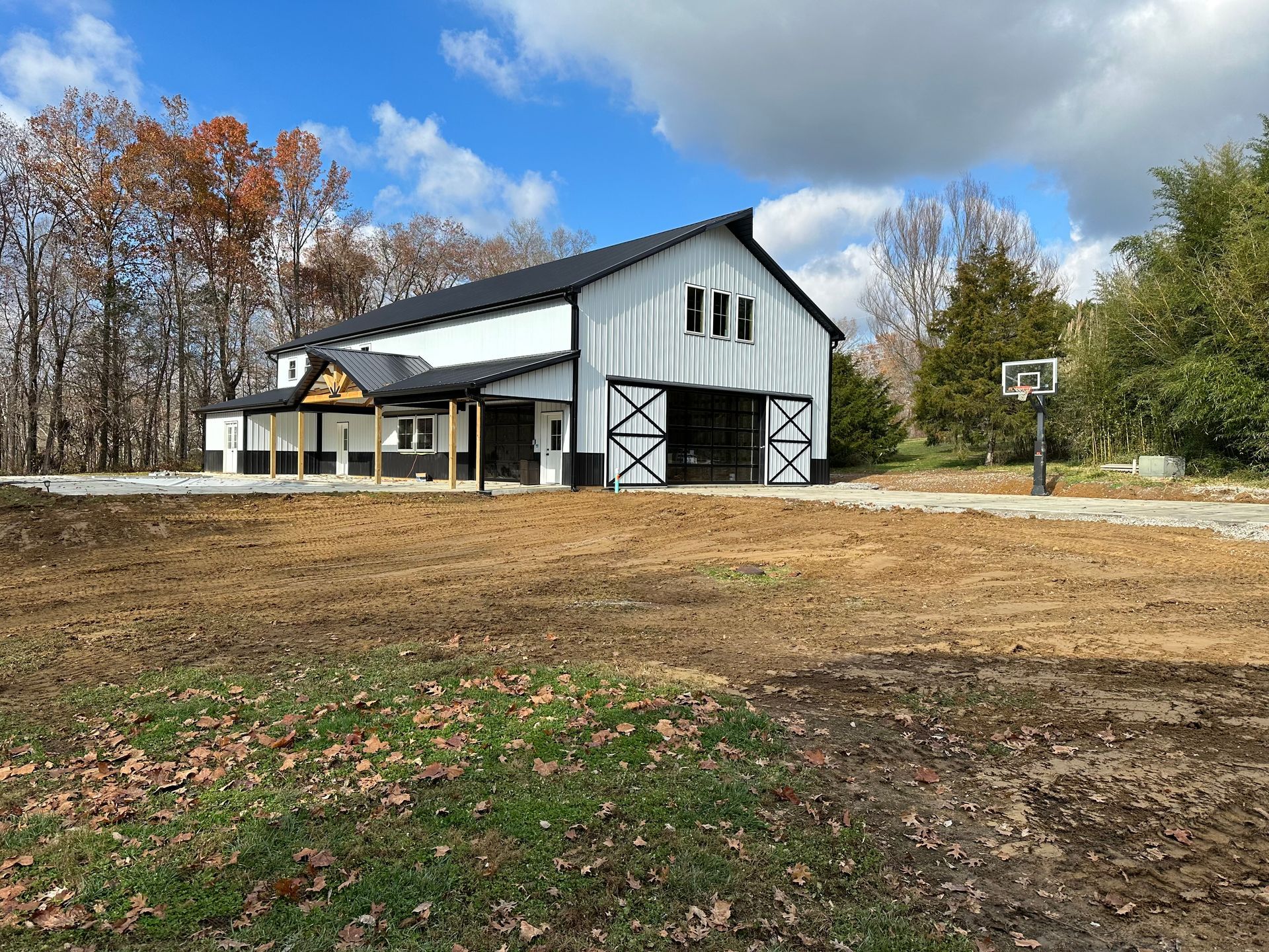 A modern, white barn-style building with black trim, a large sliding door, and a covered porch in a rural, wooded setting.
