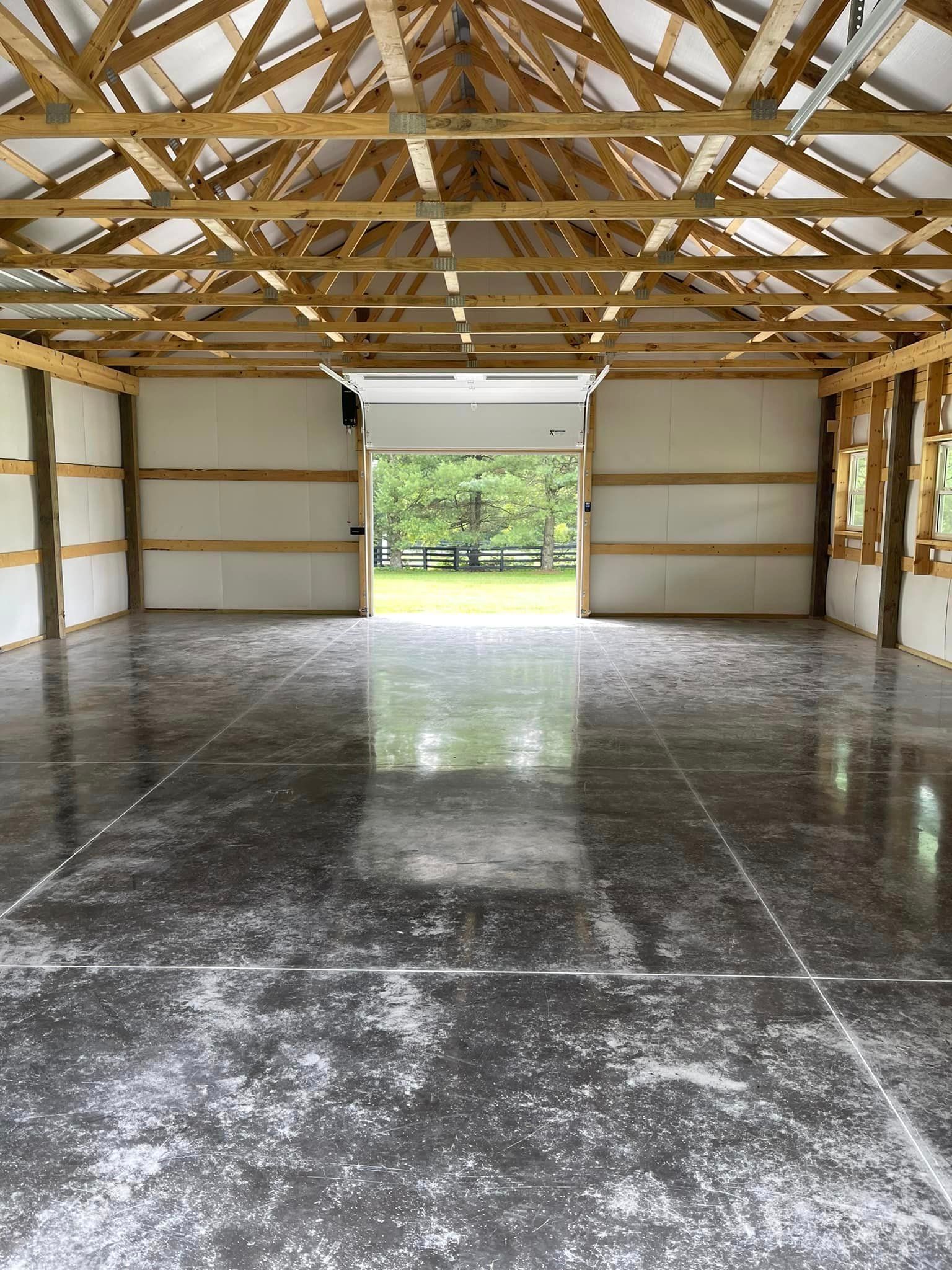An interior view of a spacious, open-frame barn with a polished concrete floor and a large open doorway looking outside.