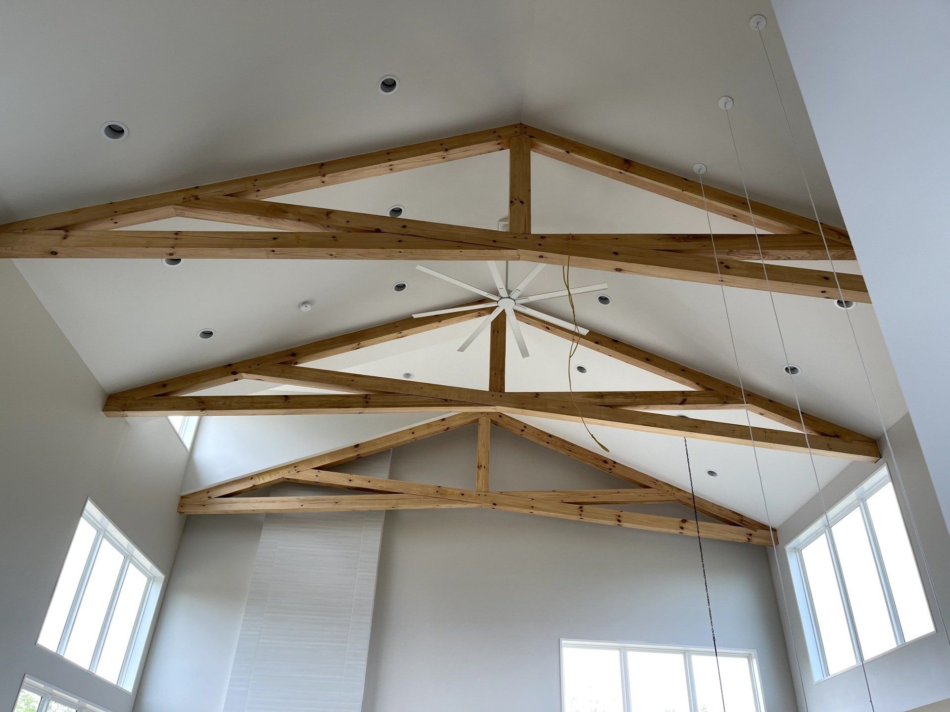 Vaulted ceiling with exposed wood trusses, recessed lighting, and a white ceiling fan in a modern, light-filled room.