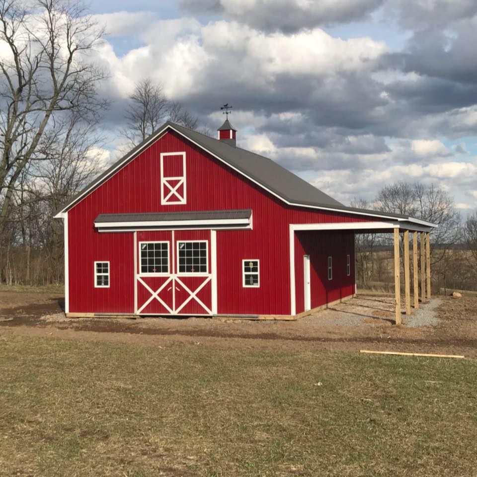 A red barn with white trim, a gabled roof, and a side porch, set in a grassy field under a cloudy sky.