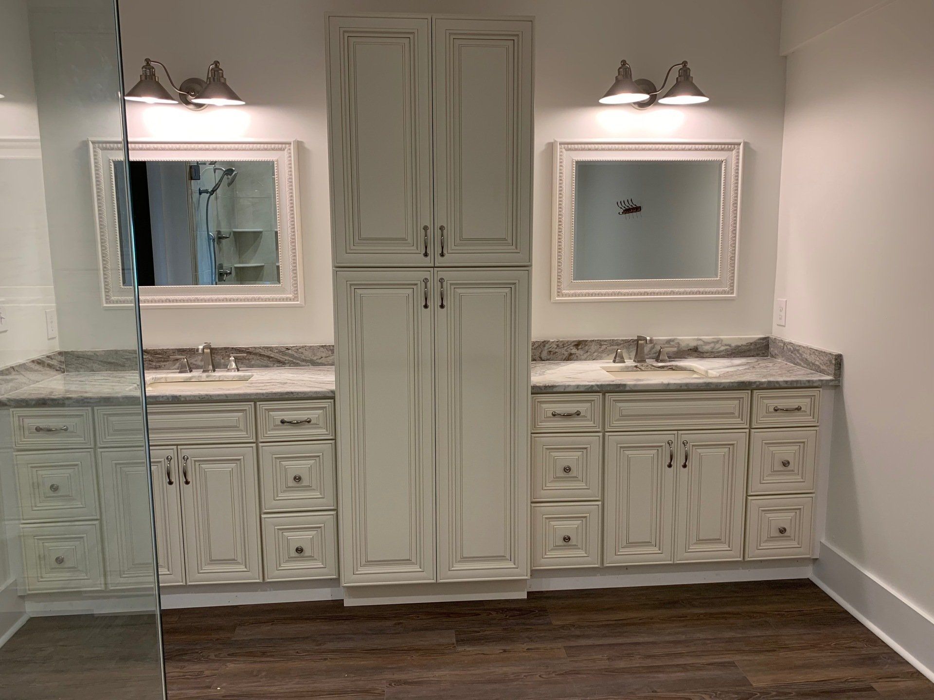 A bathroom vanity with cream-colored distressed cabinets, dual sinks, framed mirrors, and a central floor-to-ceiling tower.