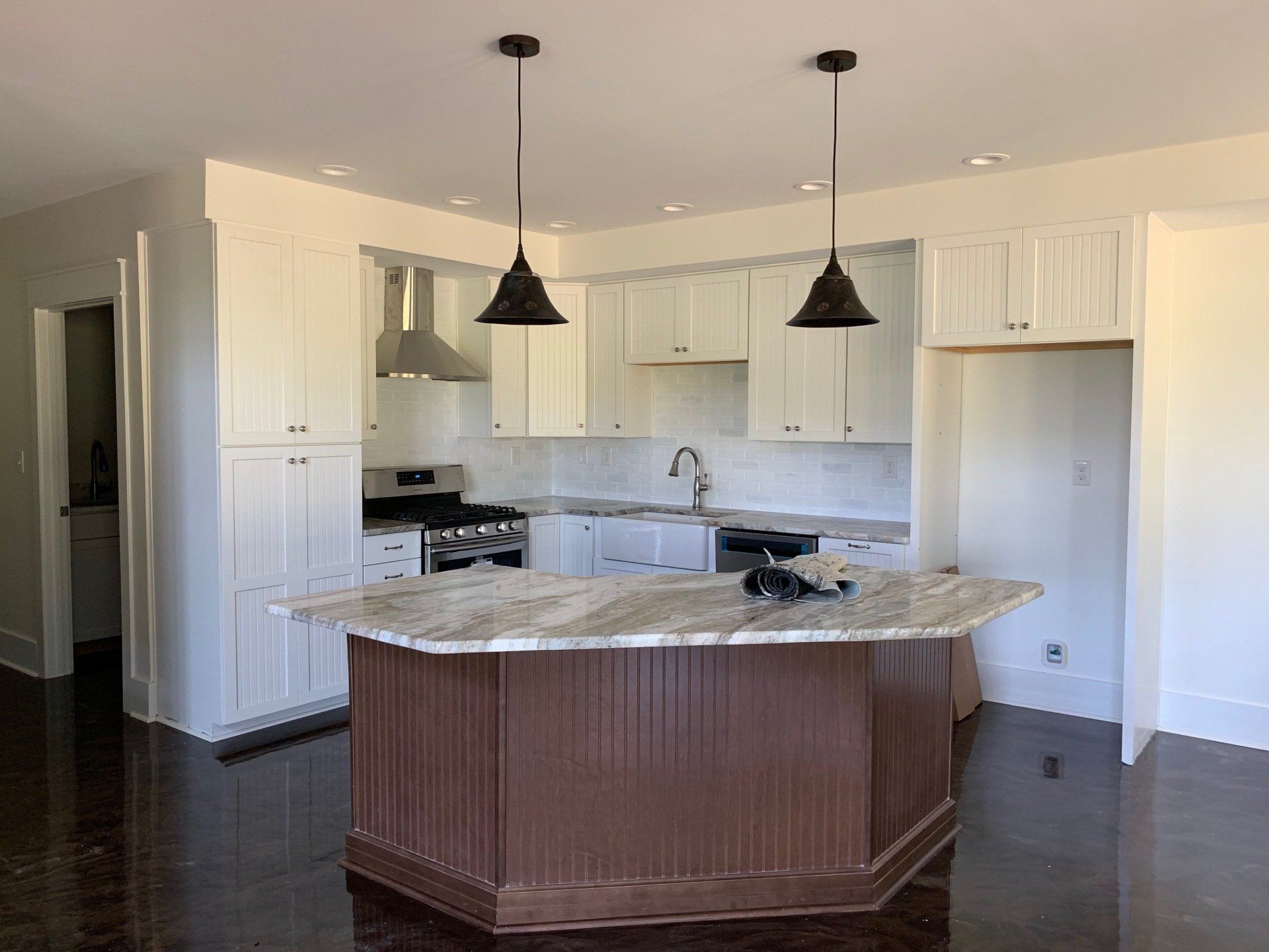 A bright kitchen features white cabinets, granite countertops, a dark brown wood island, and two pendant lights overhead.