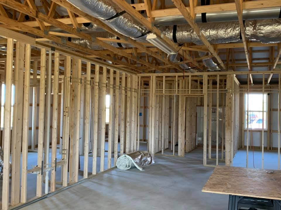 Interior view of a residential construction site featuring wood-framed walls, exposed ceiling trusses, and ductwork.