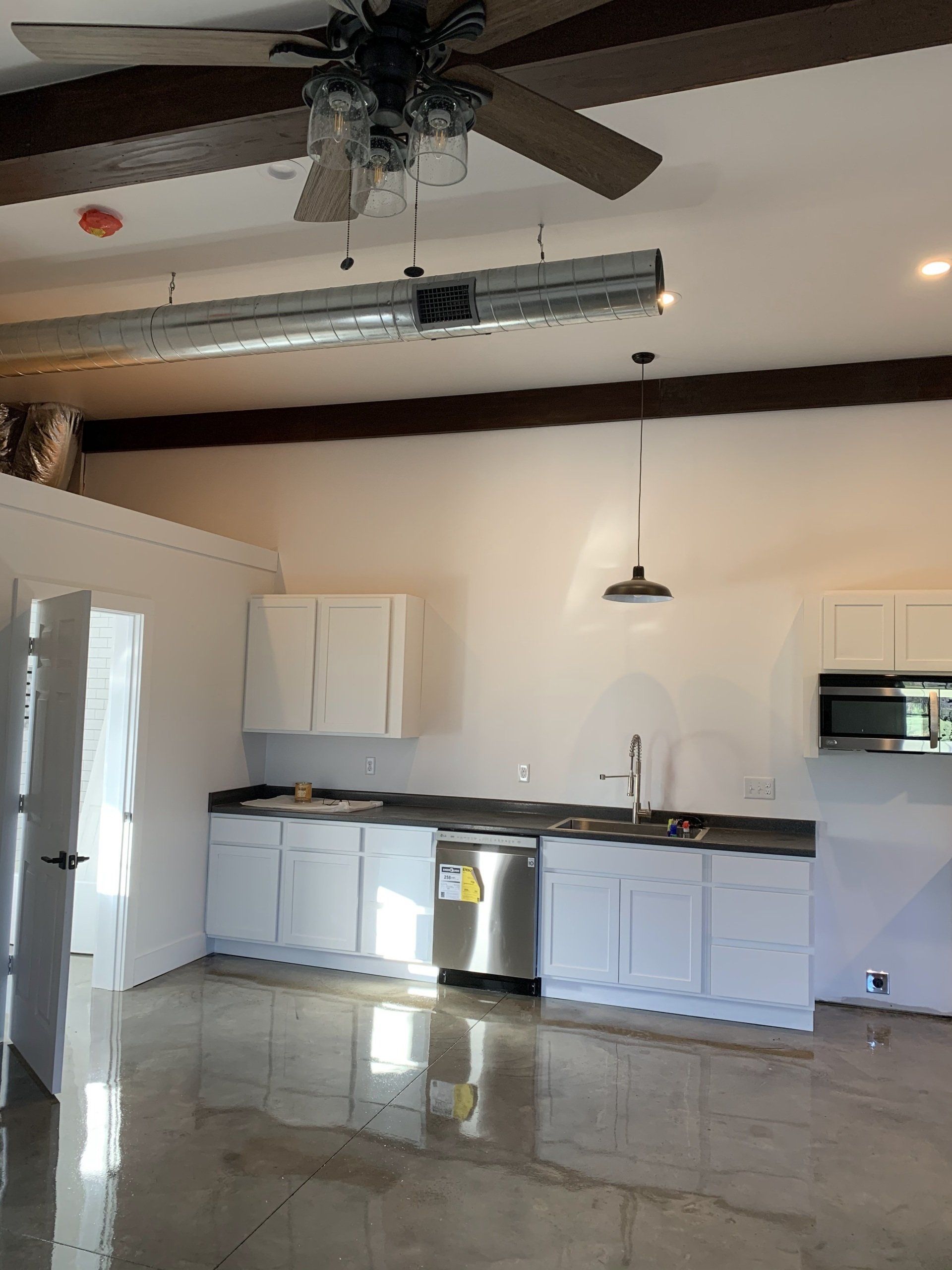 A modern, white kitchen featuring a stainless steel dishwasher, sleek cabinets, a pendant light, and a ceiling fan.