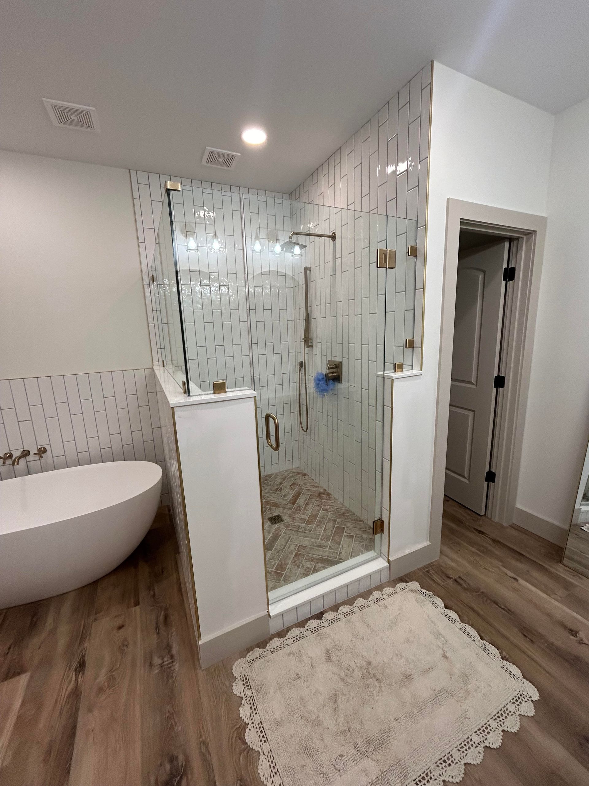 A bathroom featuring a freestanding white tub, a glass-enclosed shower with tiled walls, and wood-look flooring.