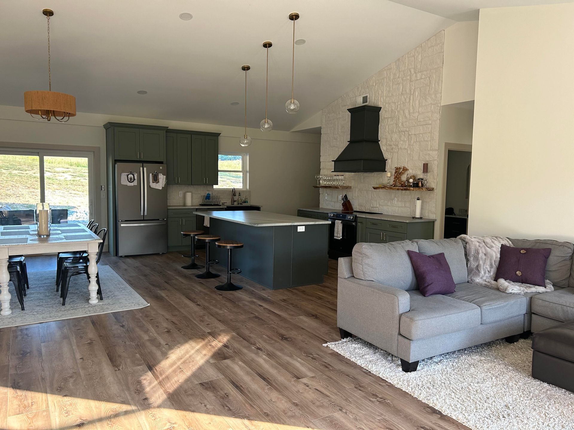 Open-concept room with a kitchen featuring dark cabinets and an island, a dining area, and a gray sectional sofa.