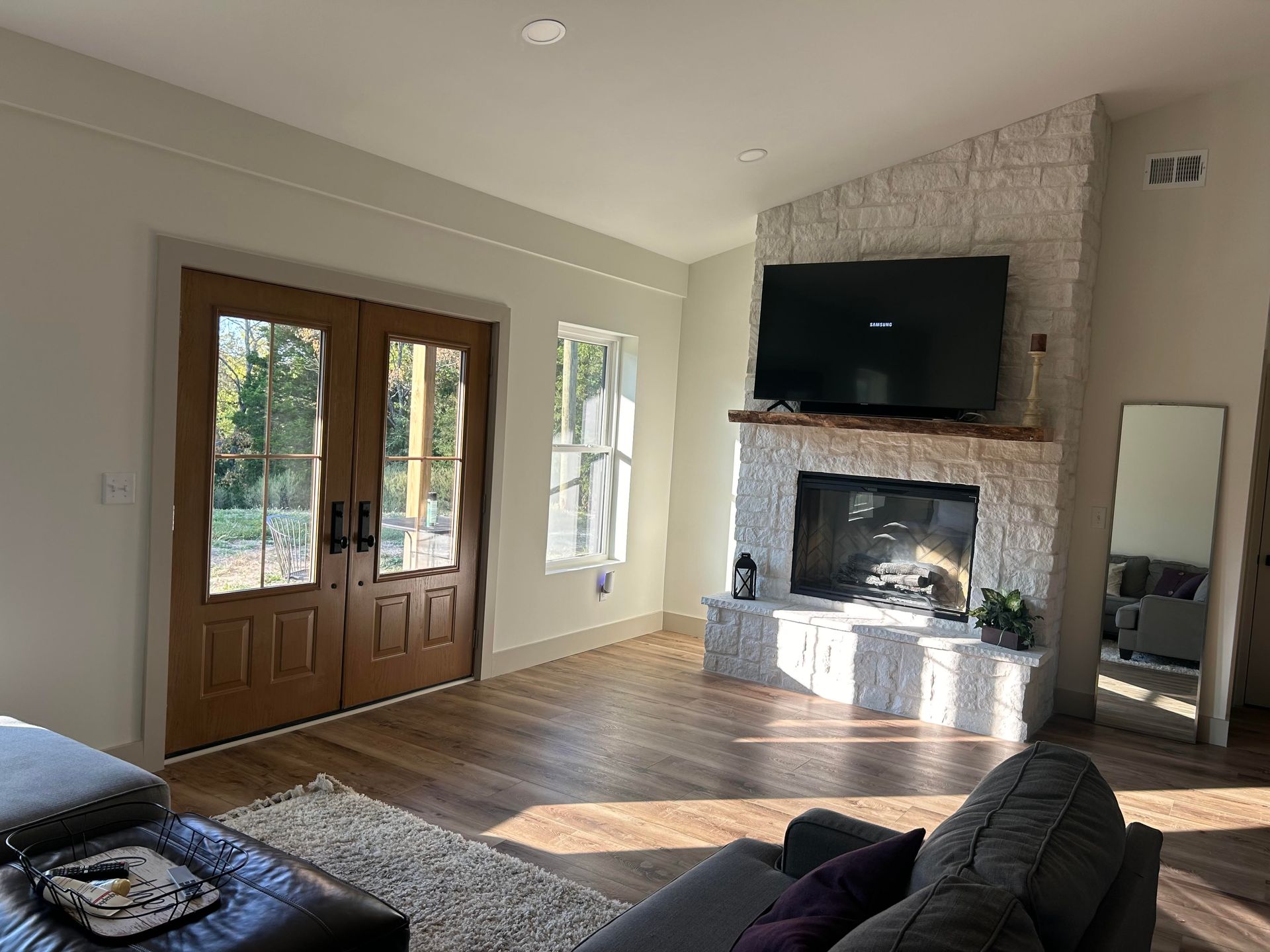 A living room featuring light-colored walls, wood floors, double doors, and a floor-to-ceiling white stone fireplace.